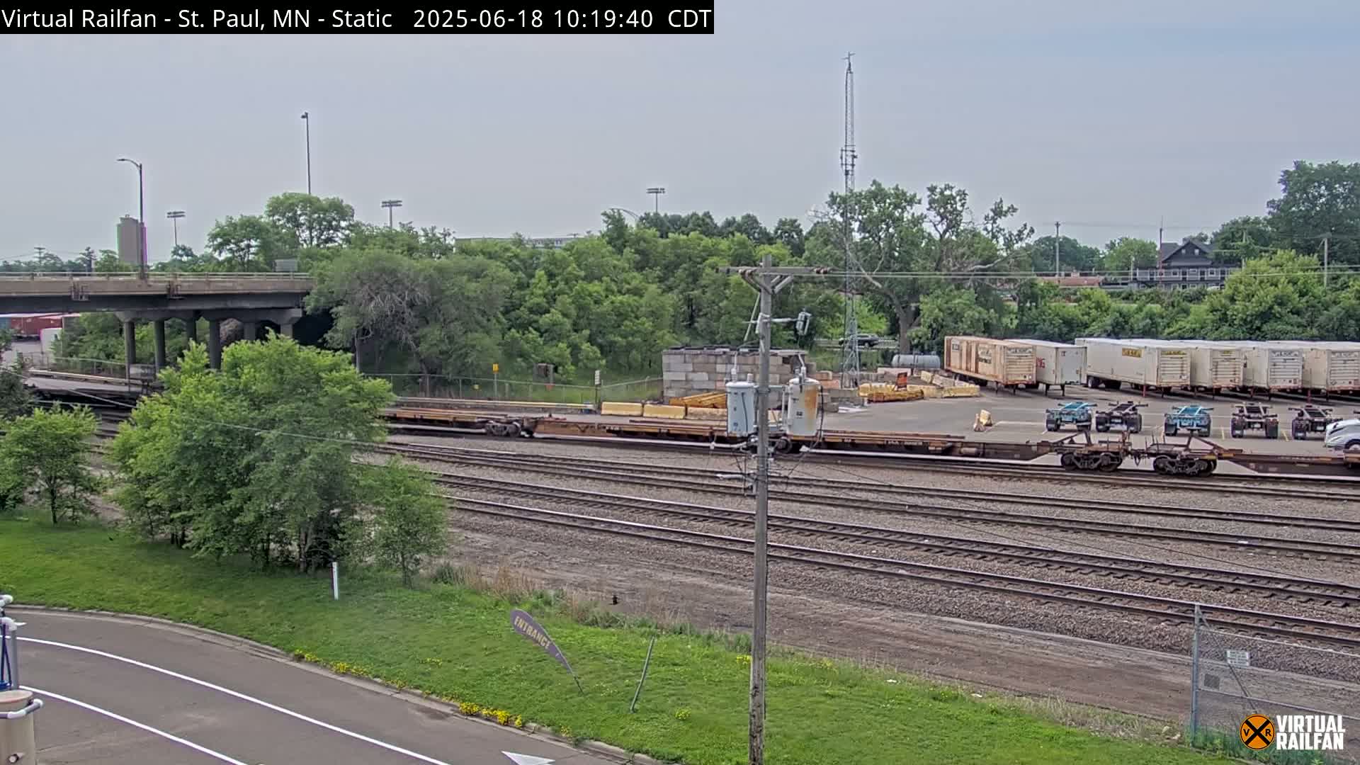 A train yard with several railcars and a road overpass under an overcast sky.
