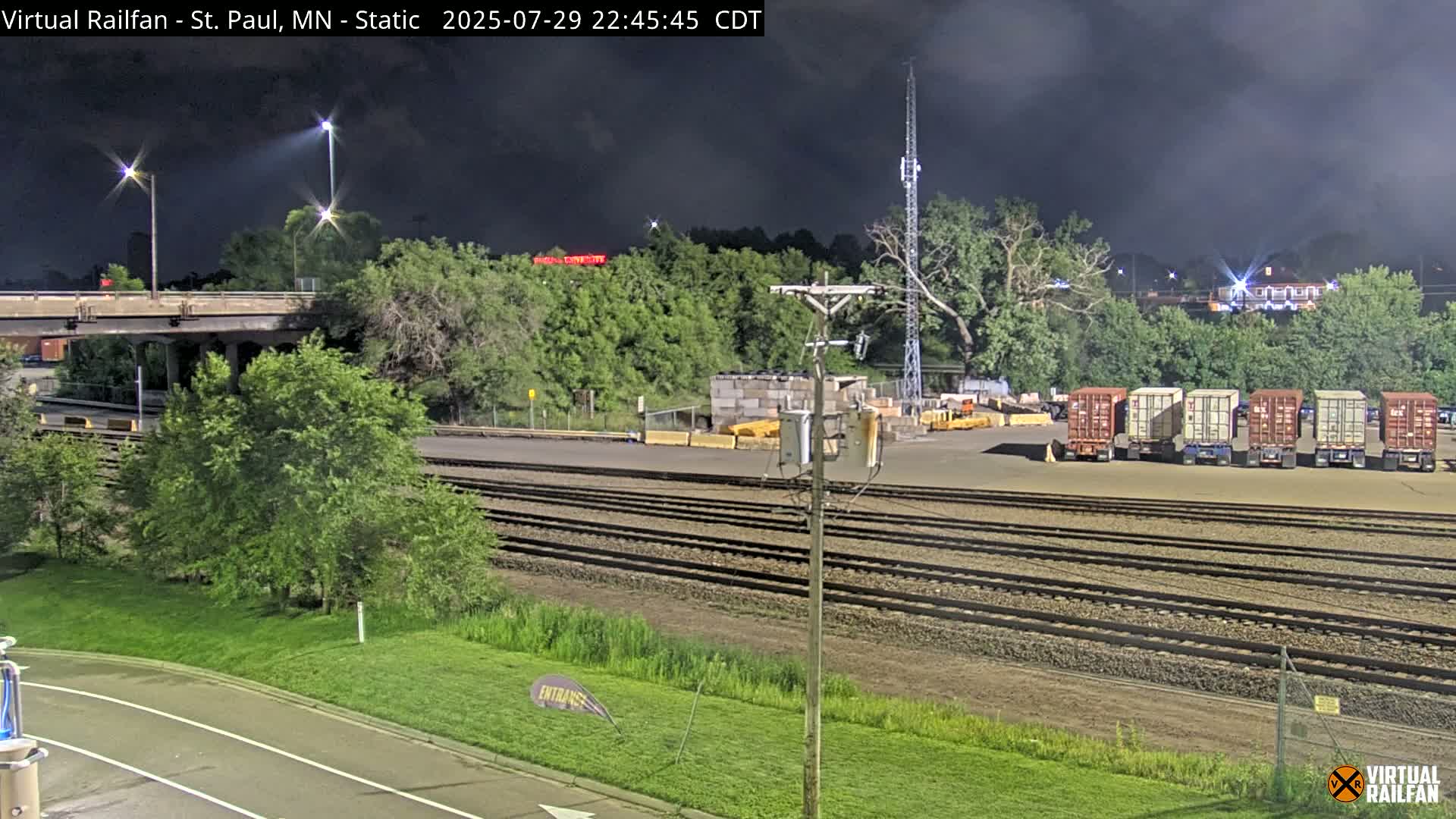 A freight train passes under a bridge at night during overcast conditions.