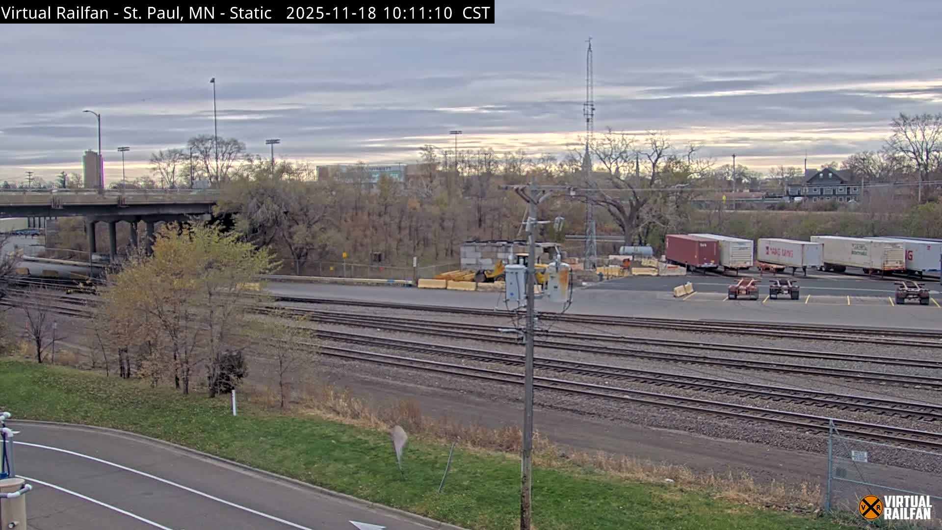 A freight train passes under a bridge at night during overcast conditions.