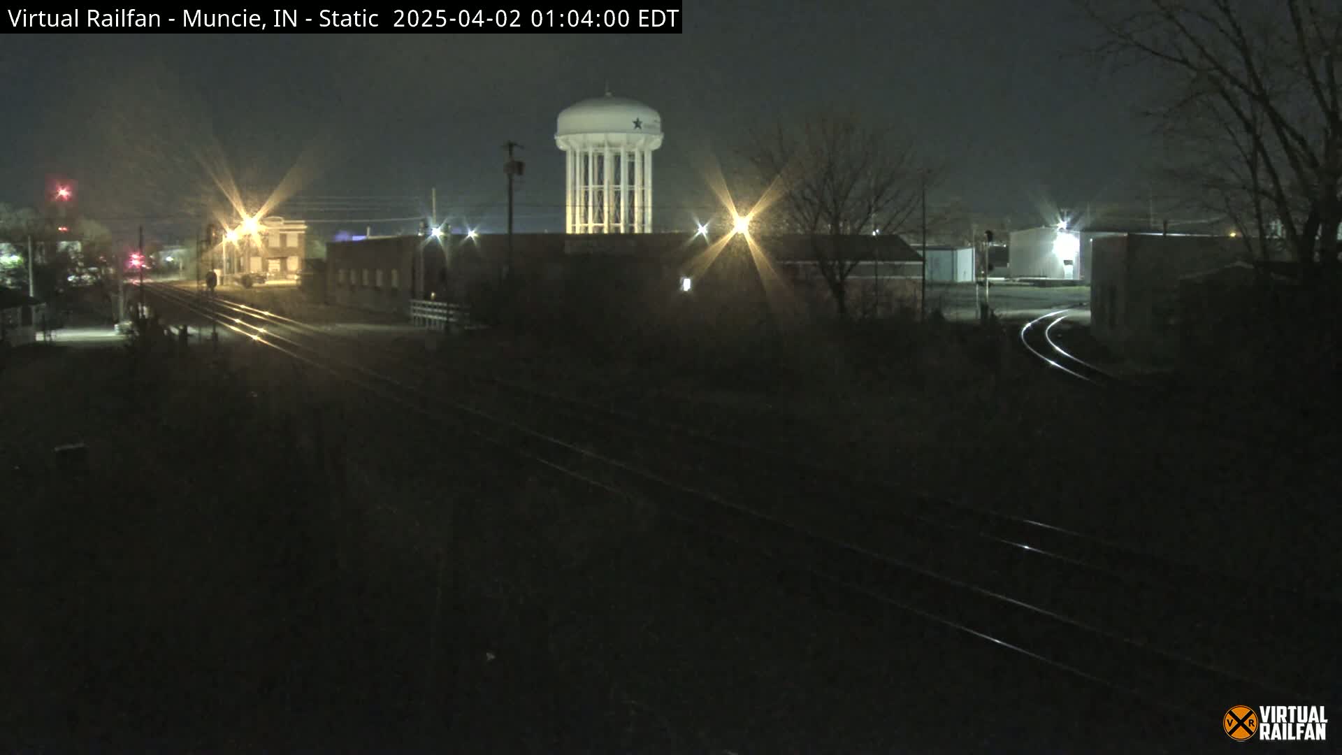 A nighttime view of a water tower and railroad tracks, illuminated by streetlights, under a clear, dark sky.