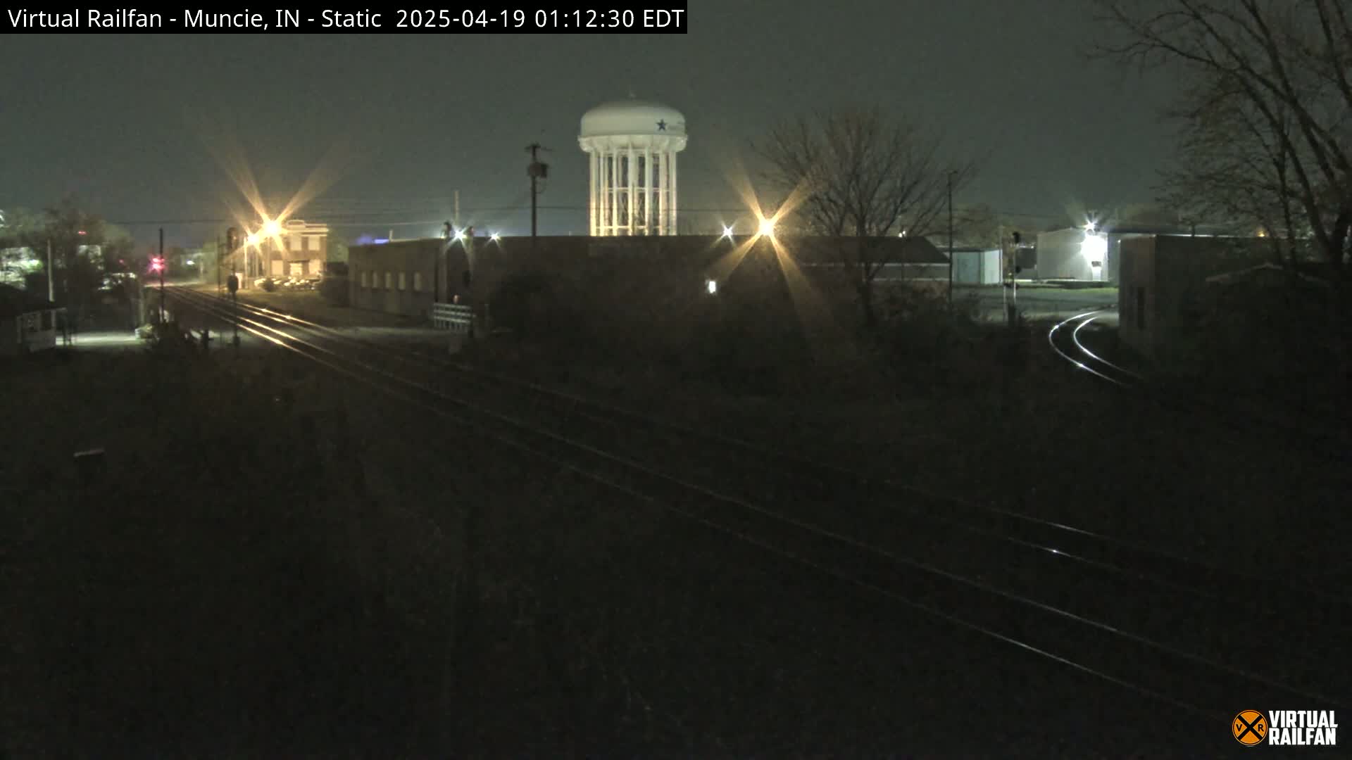 A nighttime view of railroad tracks and buildings, including a water tower, under a dark sky.