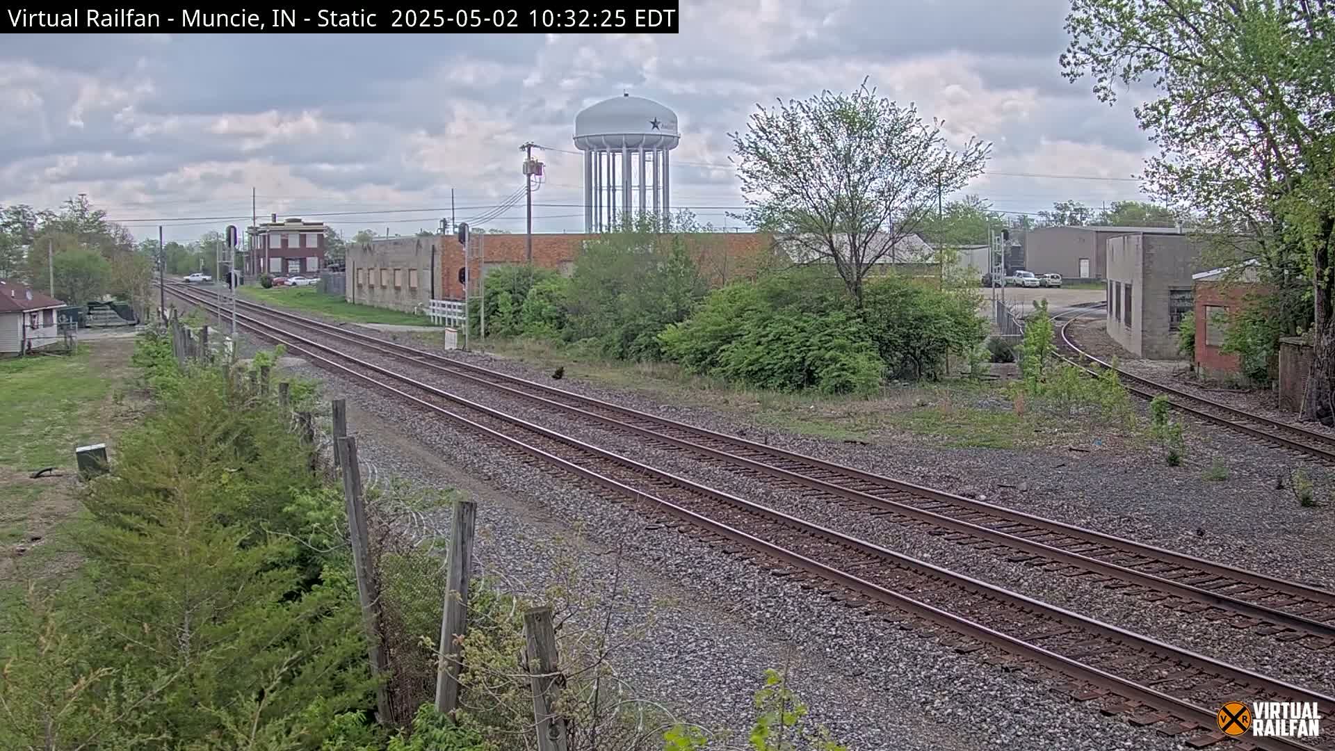 A view of train tracks on an overcast day, with buildings and a water tower visible in the background.