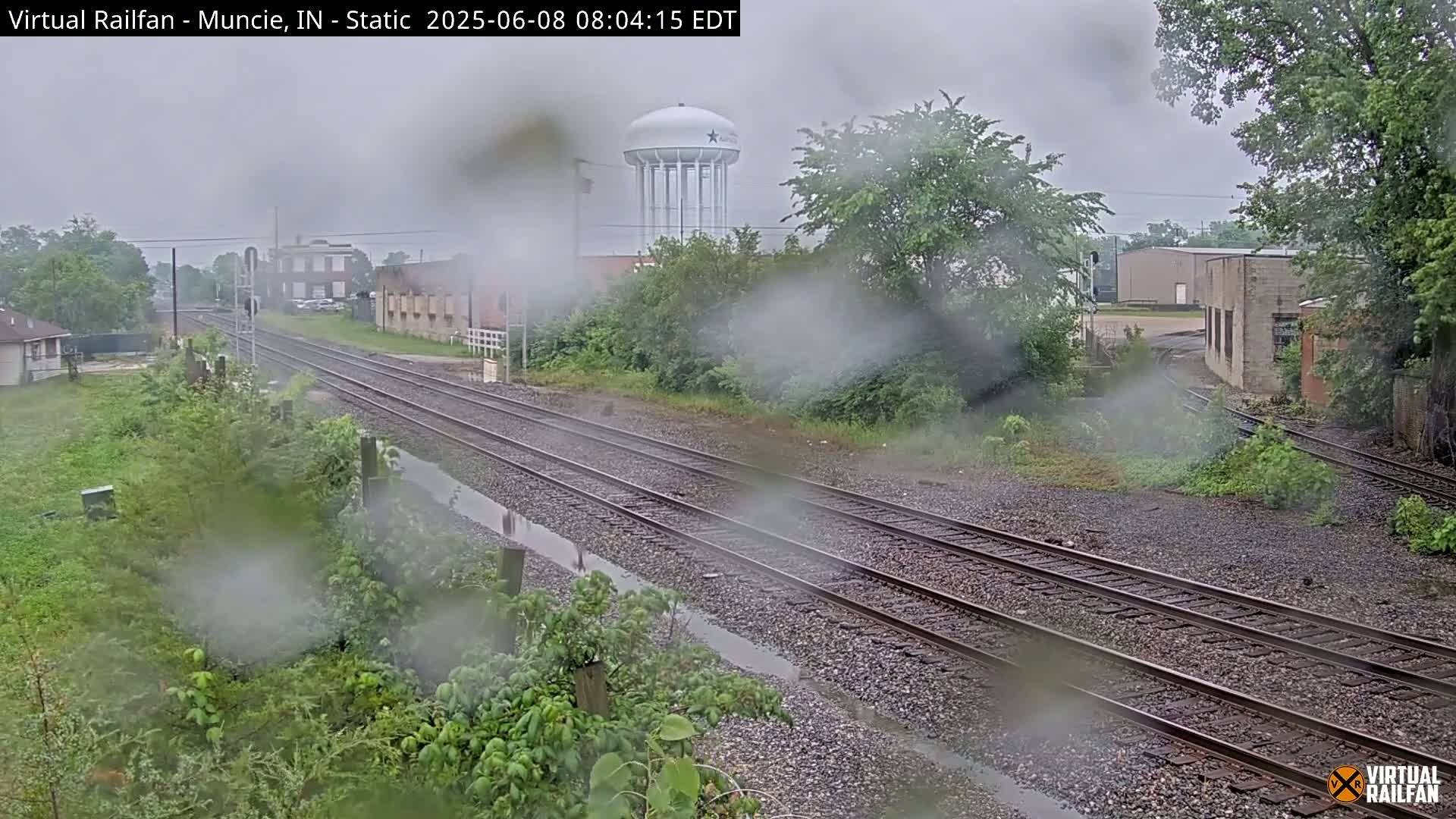 A rainy view of railroad tracks and a water tower, seen through a rain-covered surface.
