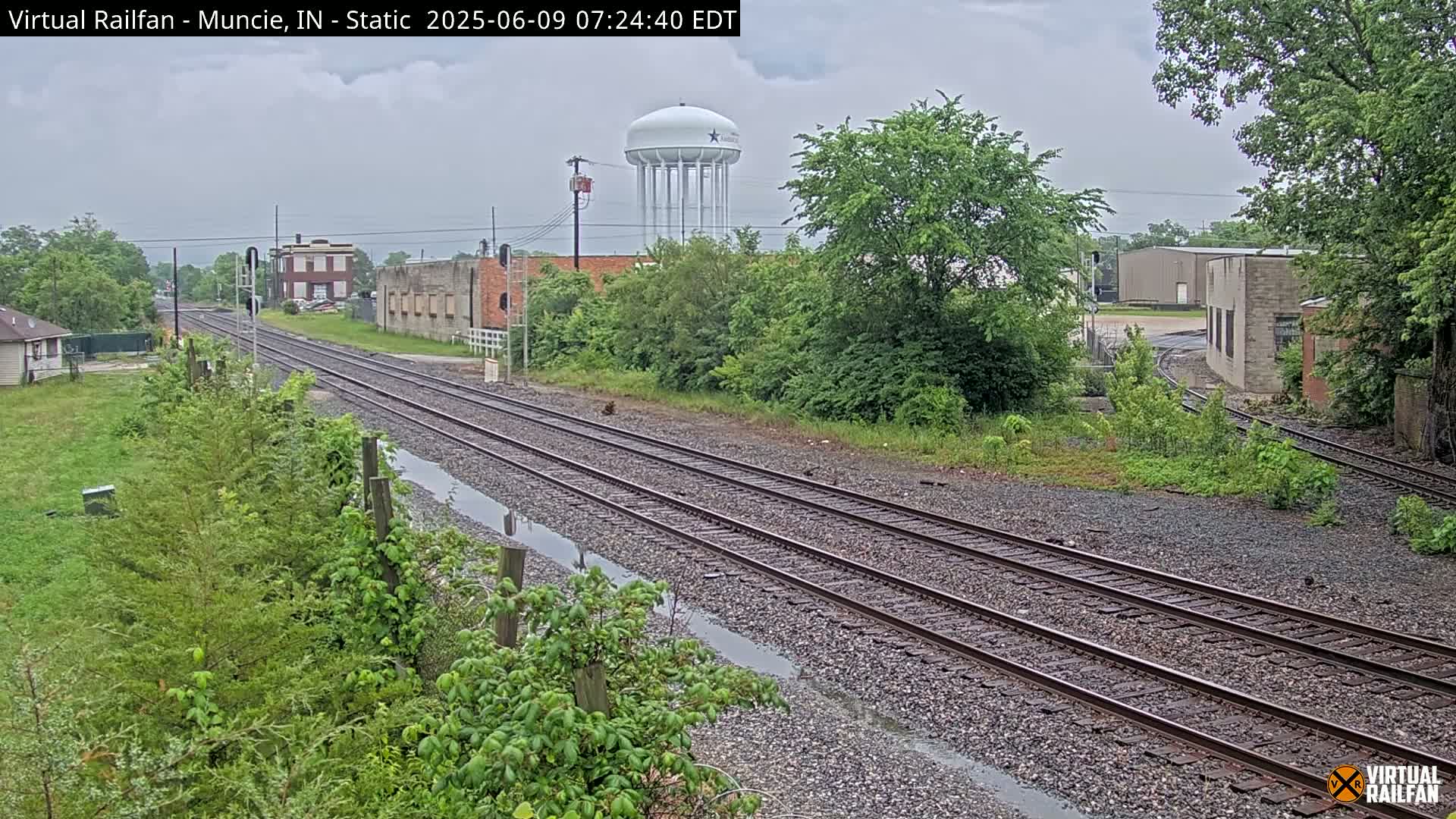 A view of railroad tracks on an overcast day, with a water tower and several buildings visible in the distance.