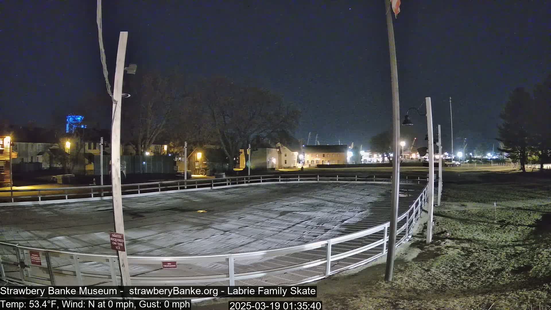 An empty outdoor ice skating rink is illuminated at night under a clear, starry sky.