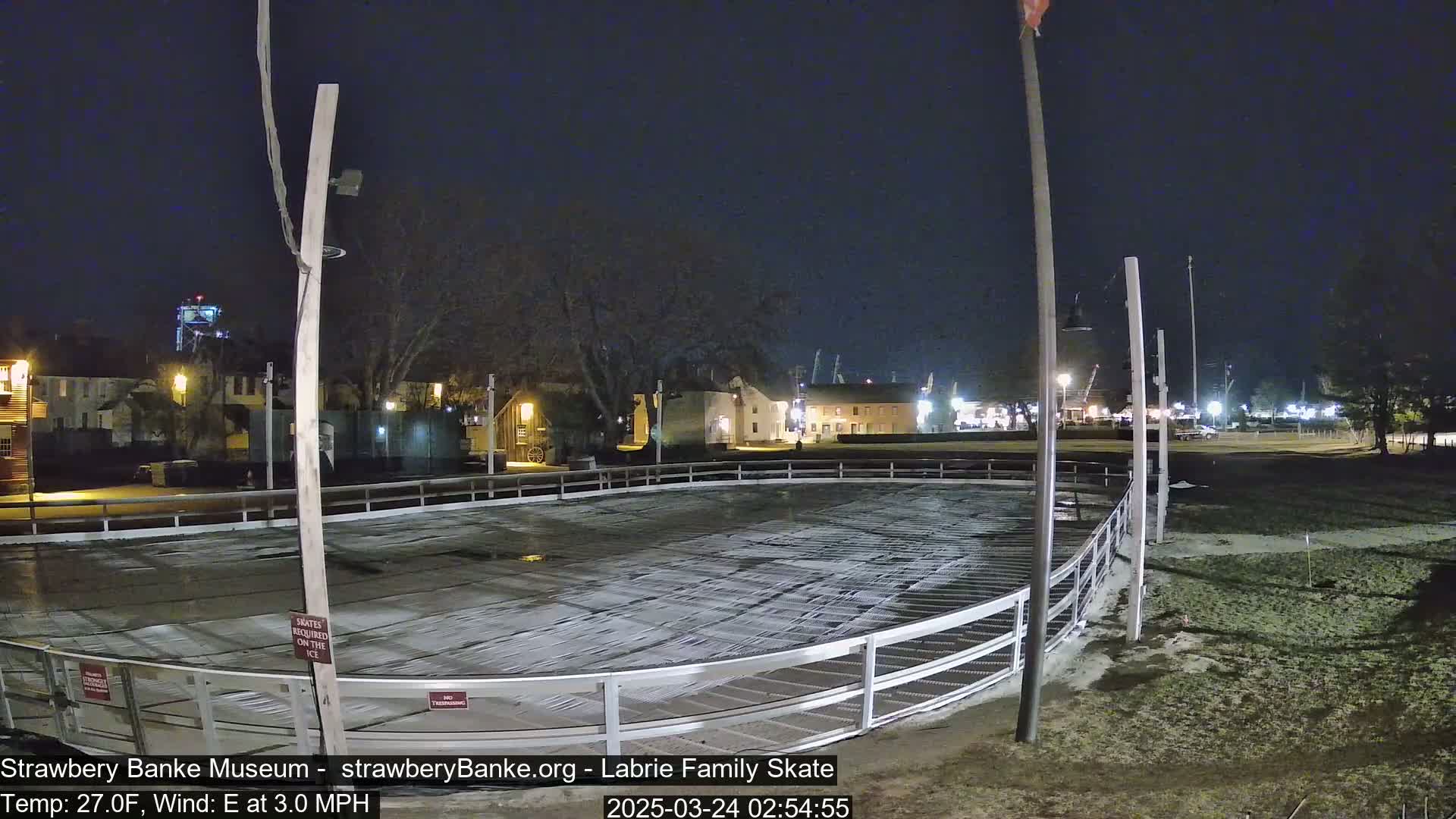 An outdoor ice skating rink at night, partially covered with snow, under a dark, clear sky with an easterly wind.