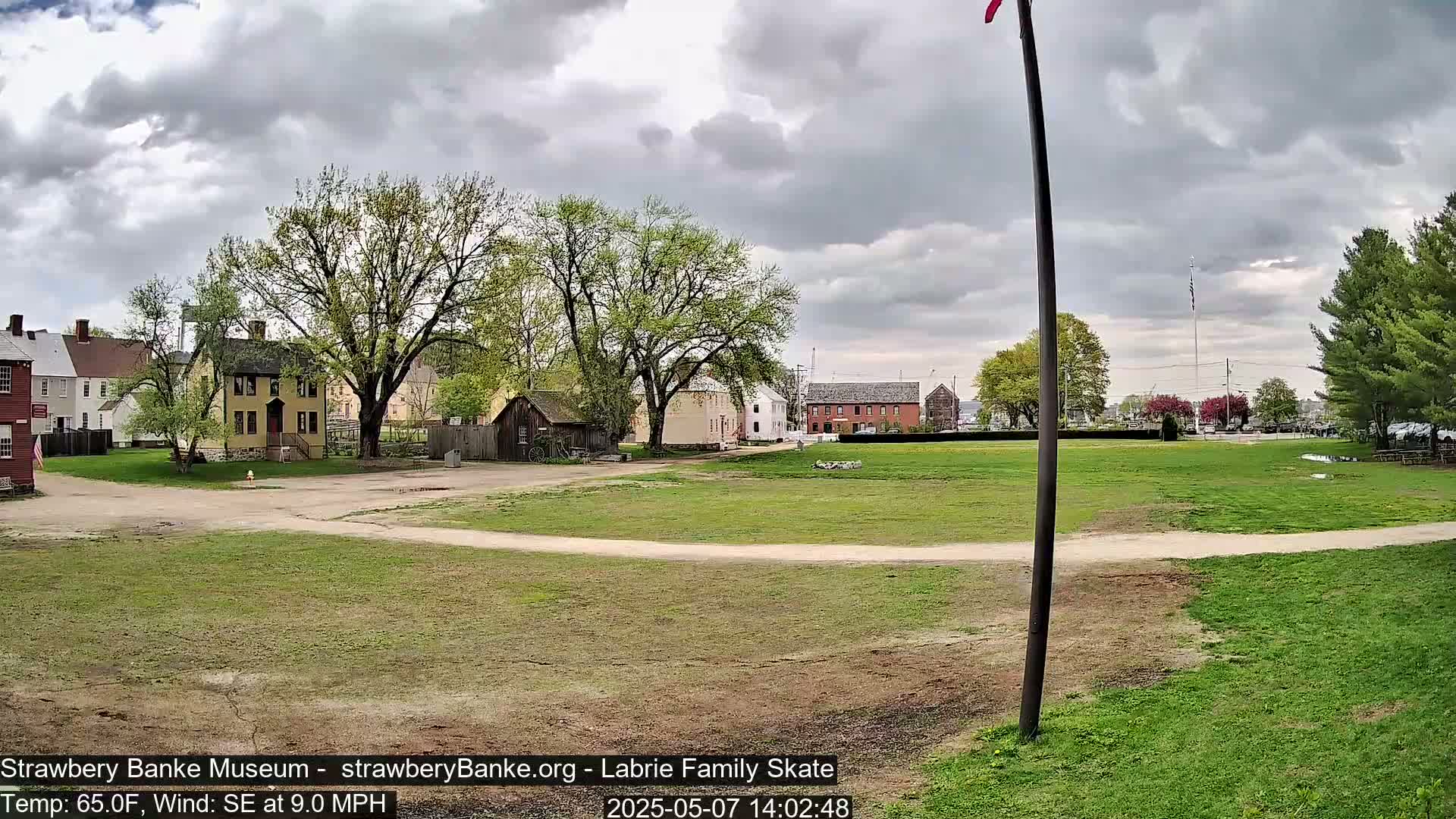 A grassy field with several historical-looking buildings in the background under a partly cloudy sky.