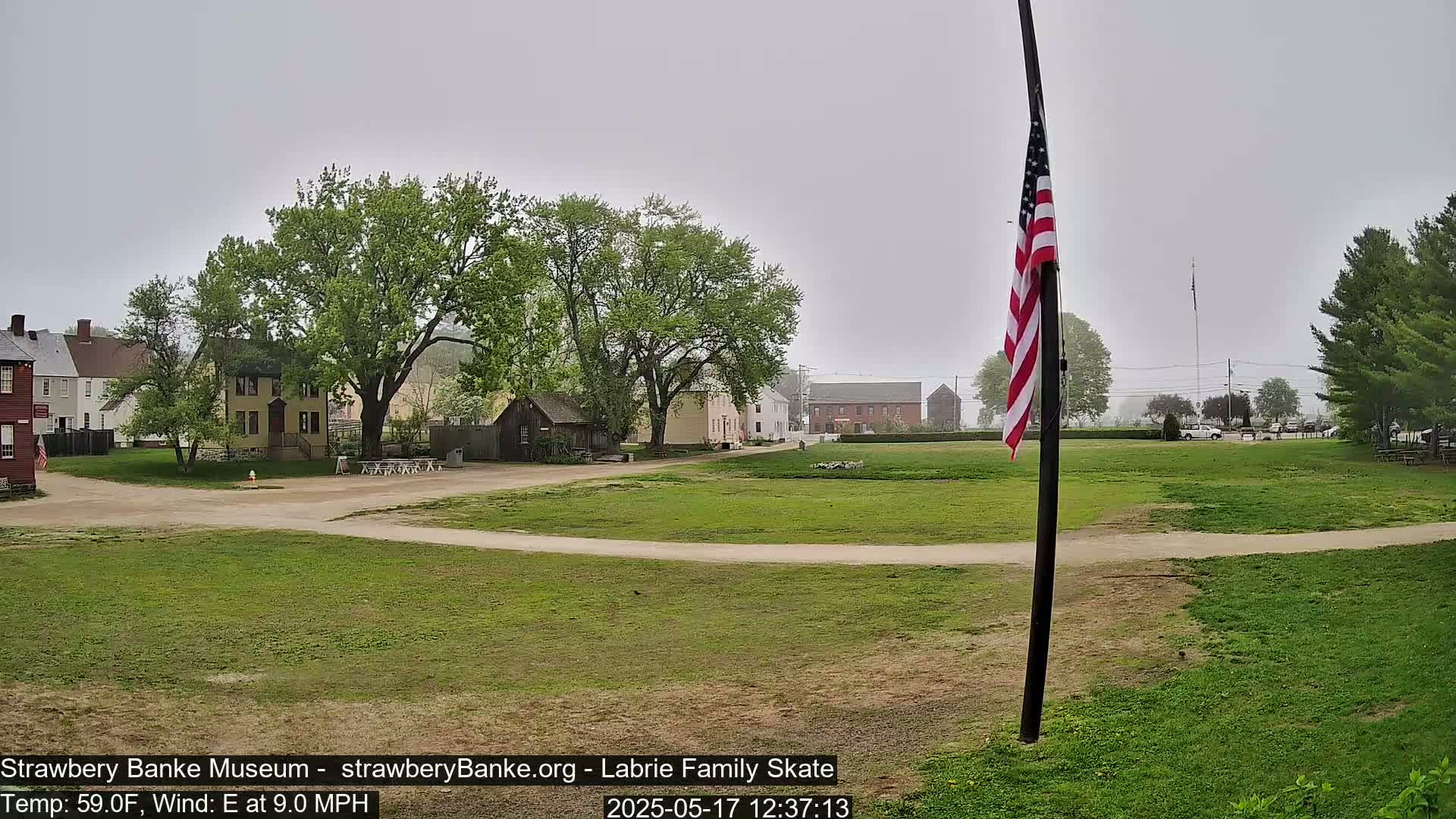 A grassy field with several historical-looking buildings in the background on an overcast day with an east wind.
