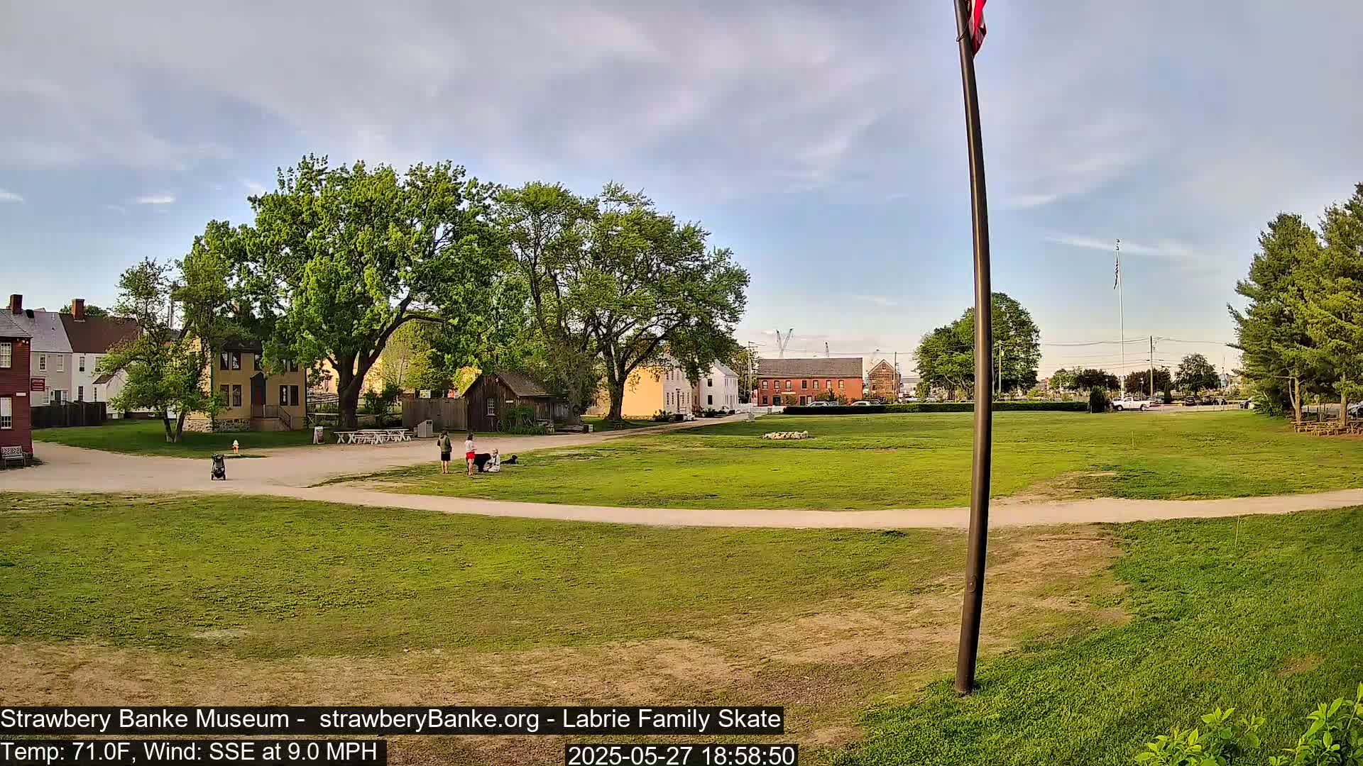 A grassy field with several historical-looking buildings in the background, under a partly cloudy sky.