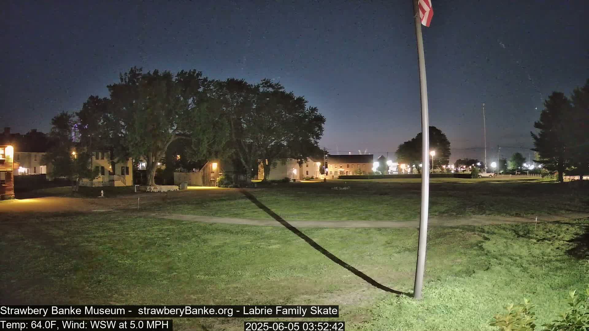 A nighttime view of a grassy area with several buildings in the background under a clear, dark sky.