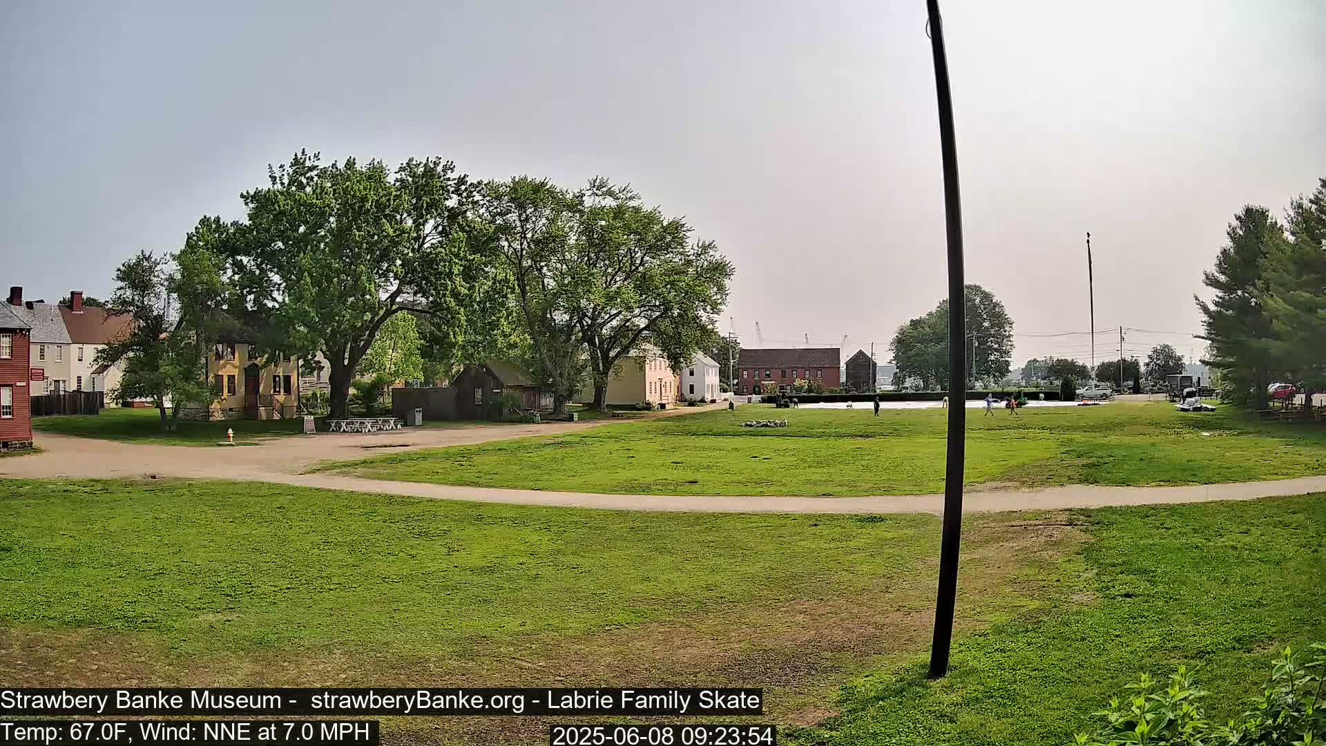 A grassy area with several historical-looking buildings and trees, under a partly cloudy sky.