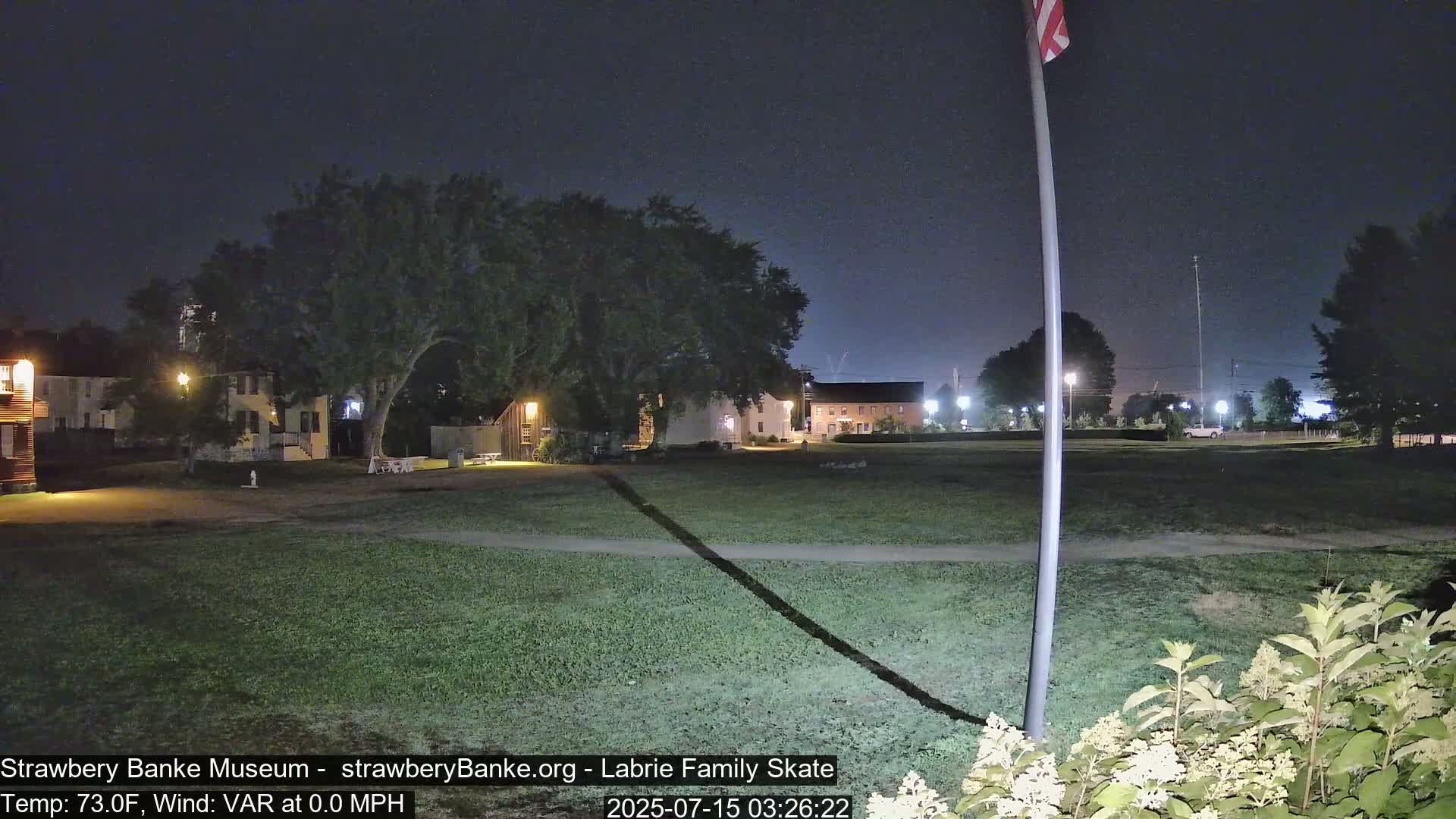 A nighttime view of a grassy area with several buildings and a flagpole, under a clear sky.