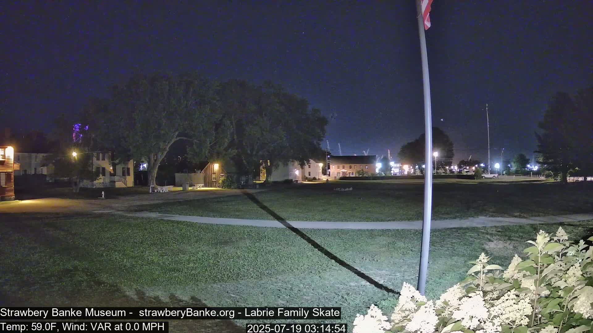A nighttime view of a grassy area with several buildings in the background under a clear, dark sky.