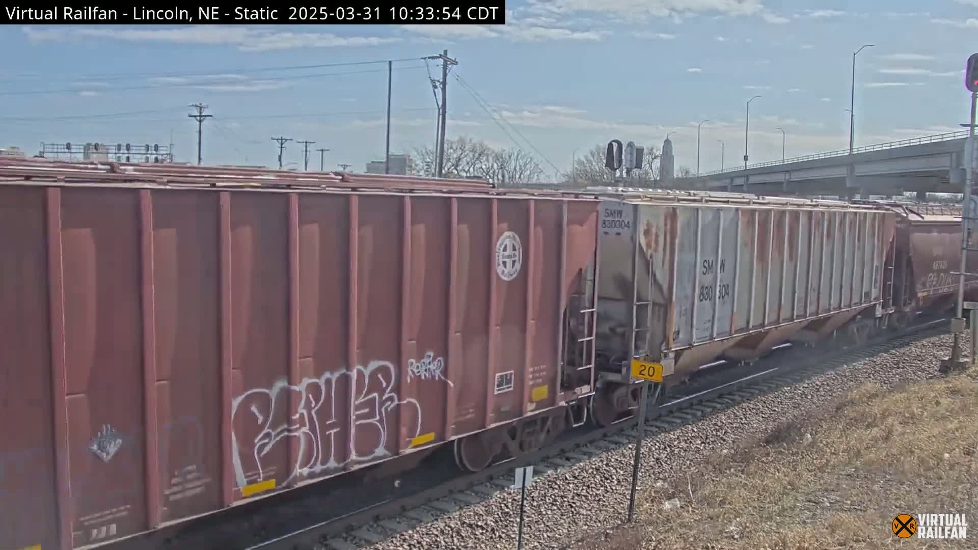 A long freight train with graffiti on some of its cars moves along a track under a partly cloudy sky.