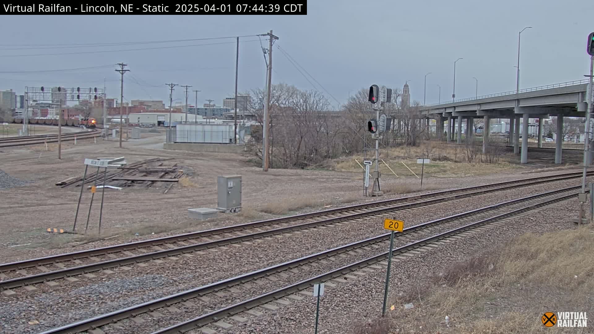A train passes by a railway crossing under an overpass on an overcast day.