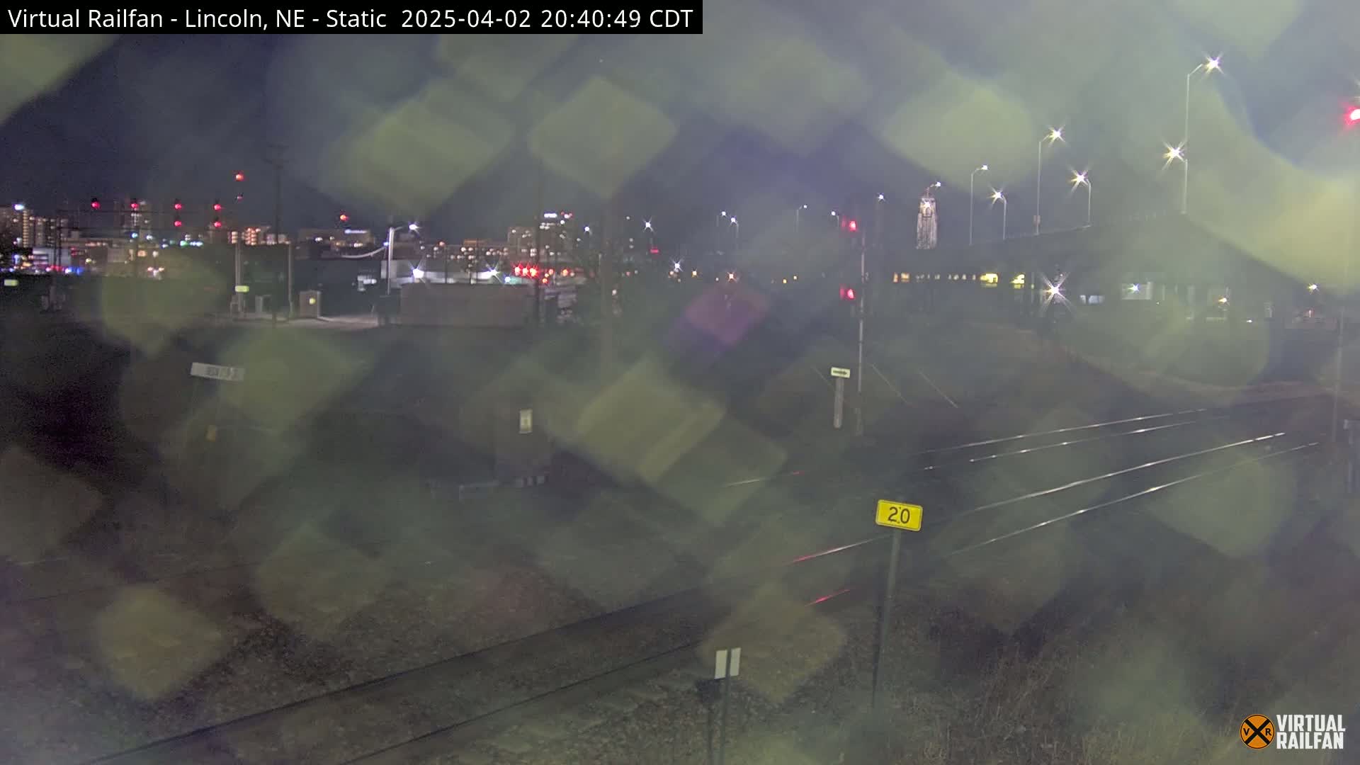 A nighttime view of railroad tracks and a city skyline in the distance, under hazy conditions.