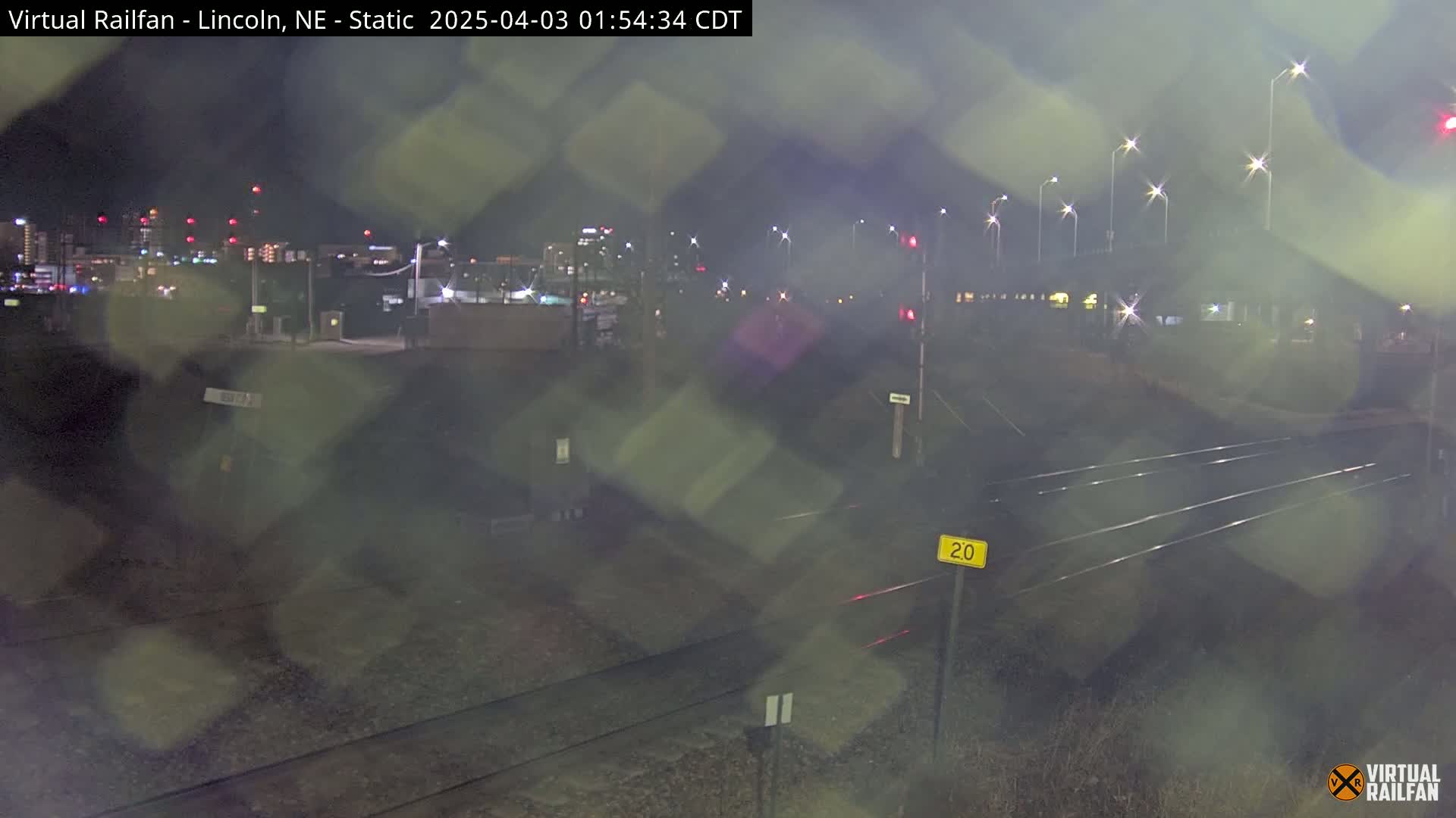 A nighttime view of railroad tracks near a city skyline, under hazy conditions.