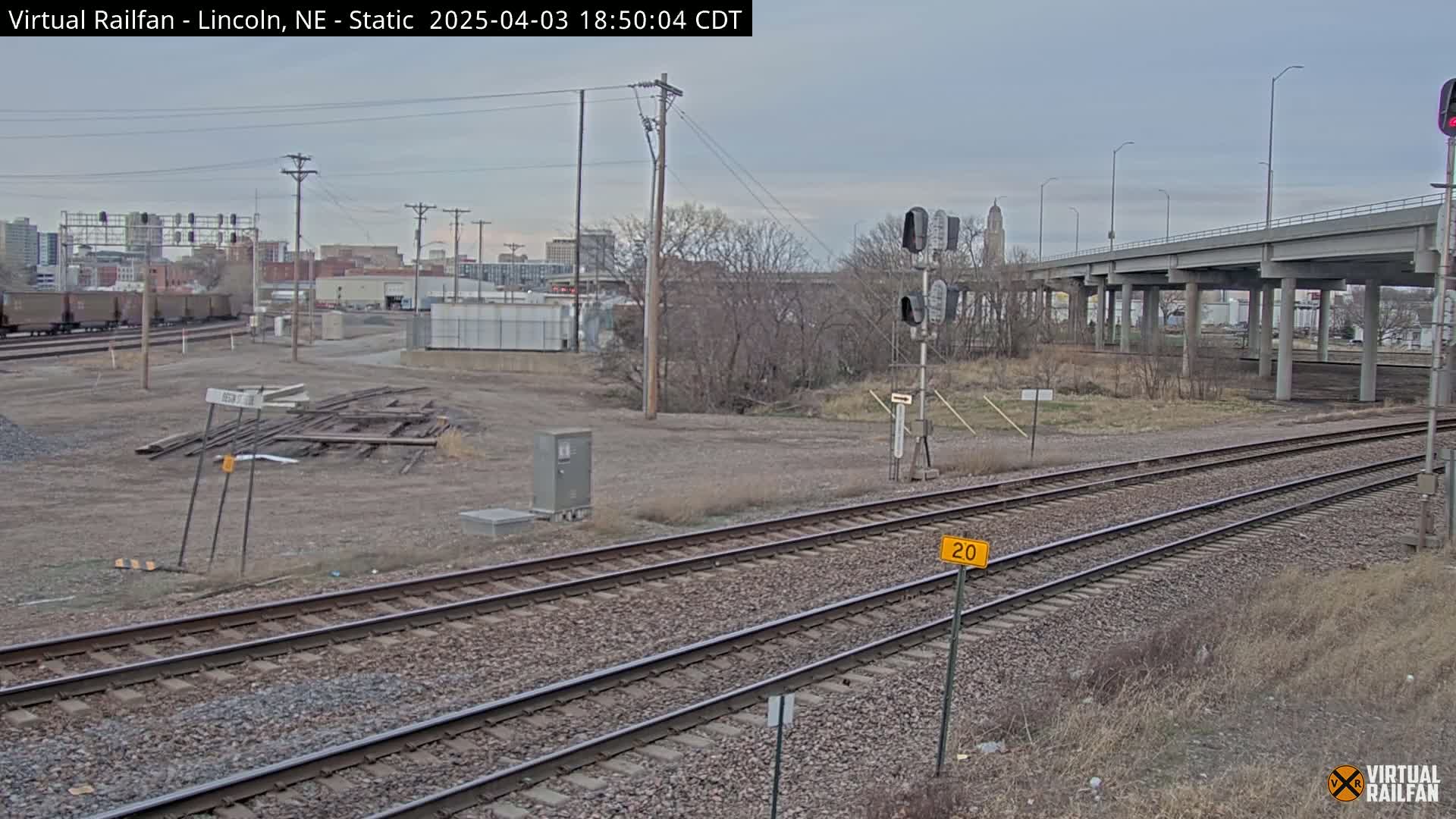 A view of railroad tracks and a large overpass on an overcast day, with a city skyline in the background.
