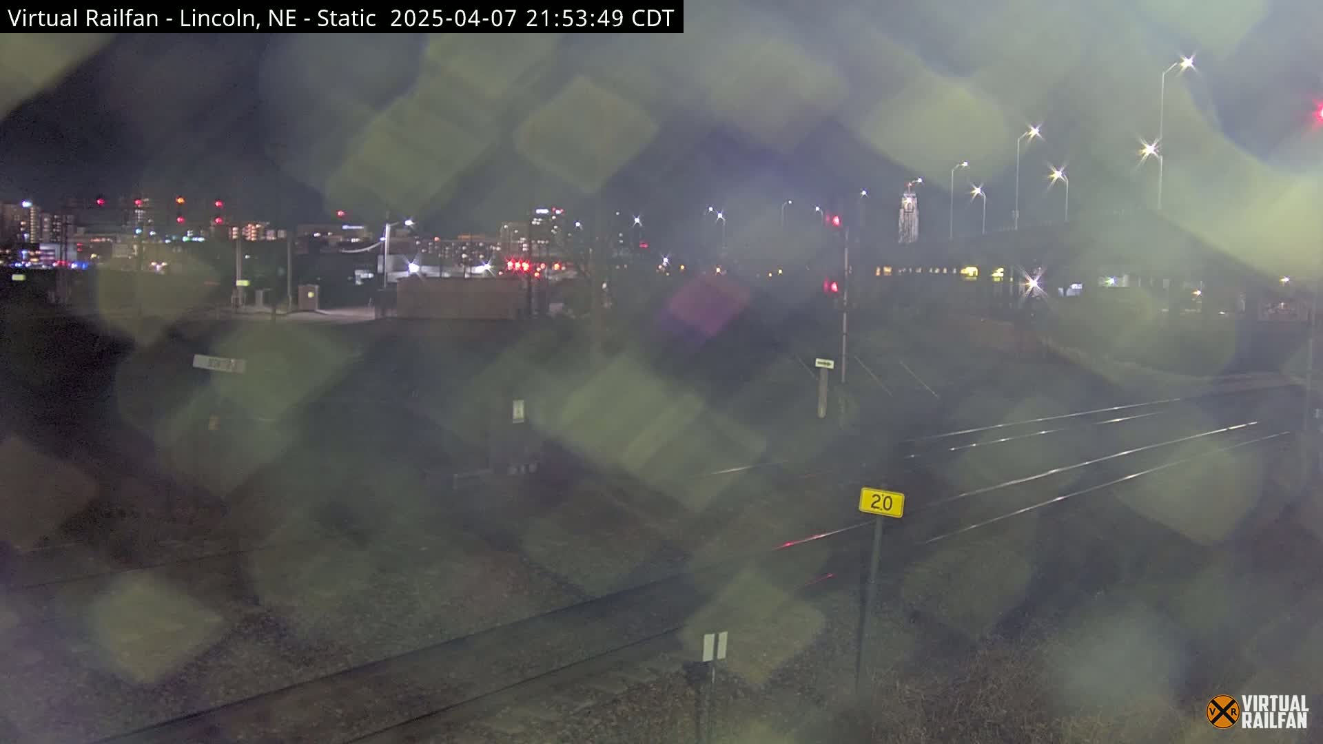 A nighttime view of train tracks and a city skyline in the distance, with rain obscuring the view.