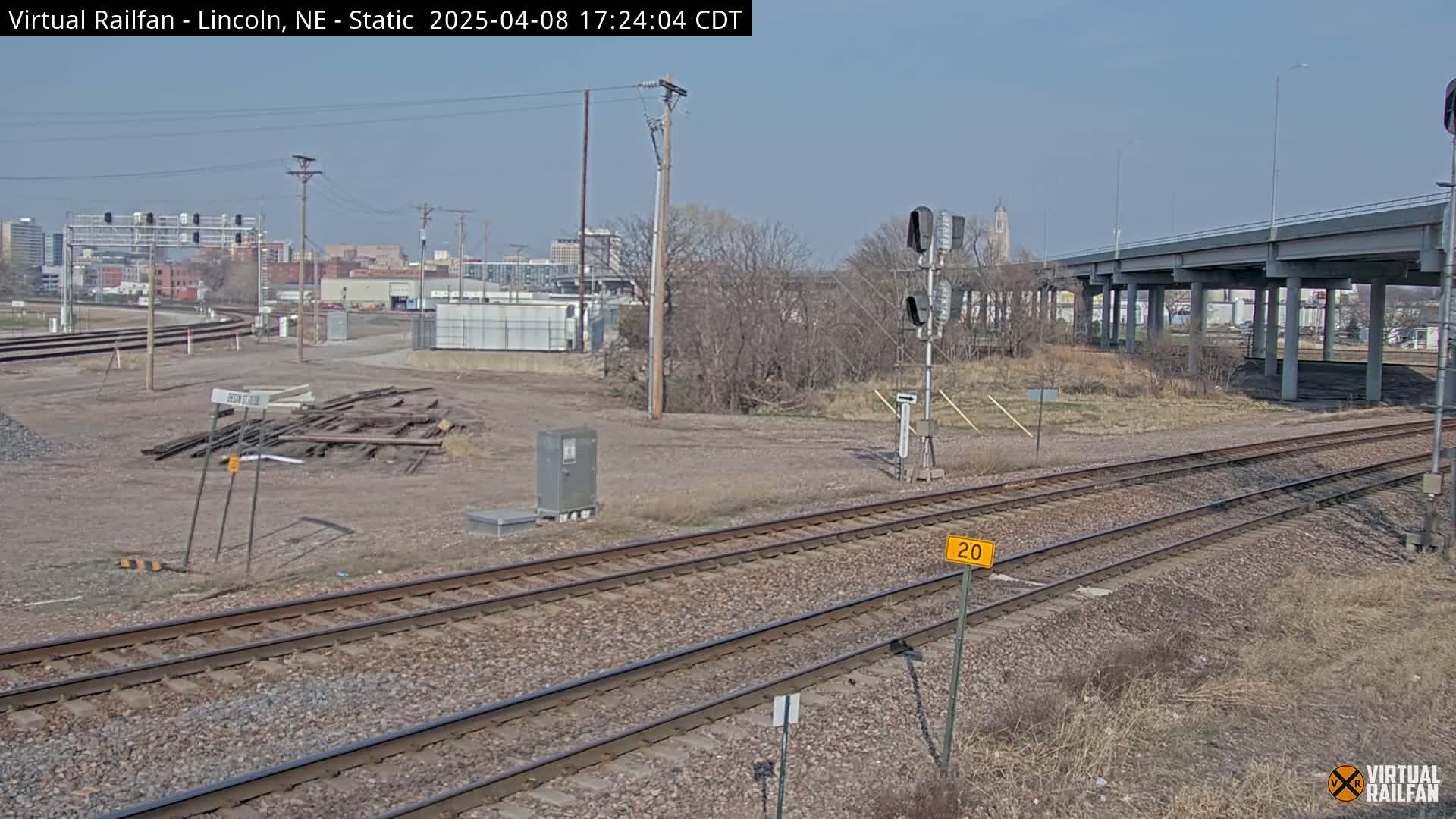A mostly clear day view of railroad tracks and a pile of discarded railroad ties, with a city skyline in the background.