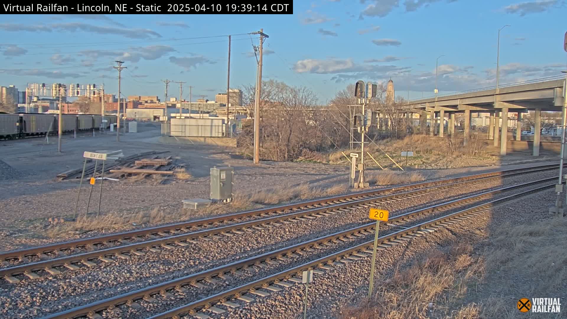 Railroad tracks and a nearby elevated roadway are visible under a partly cloudy sky.