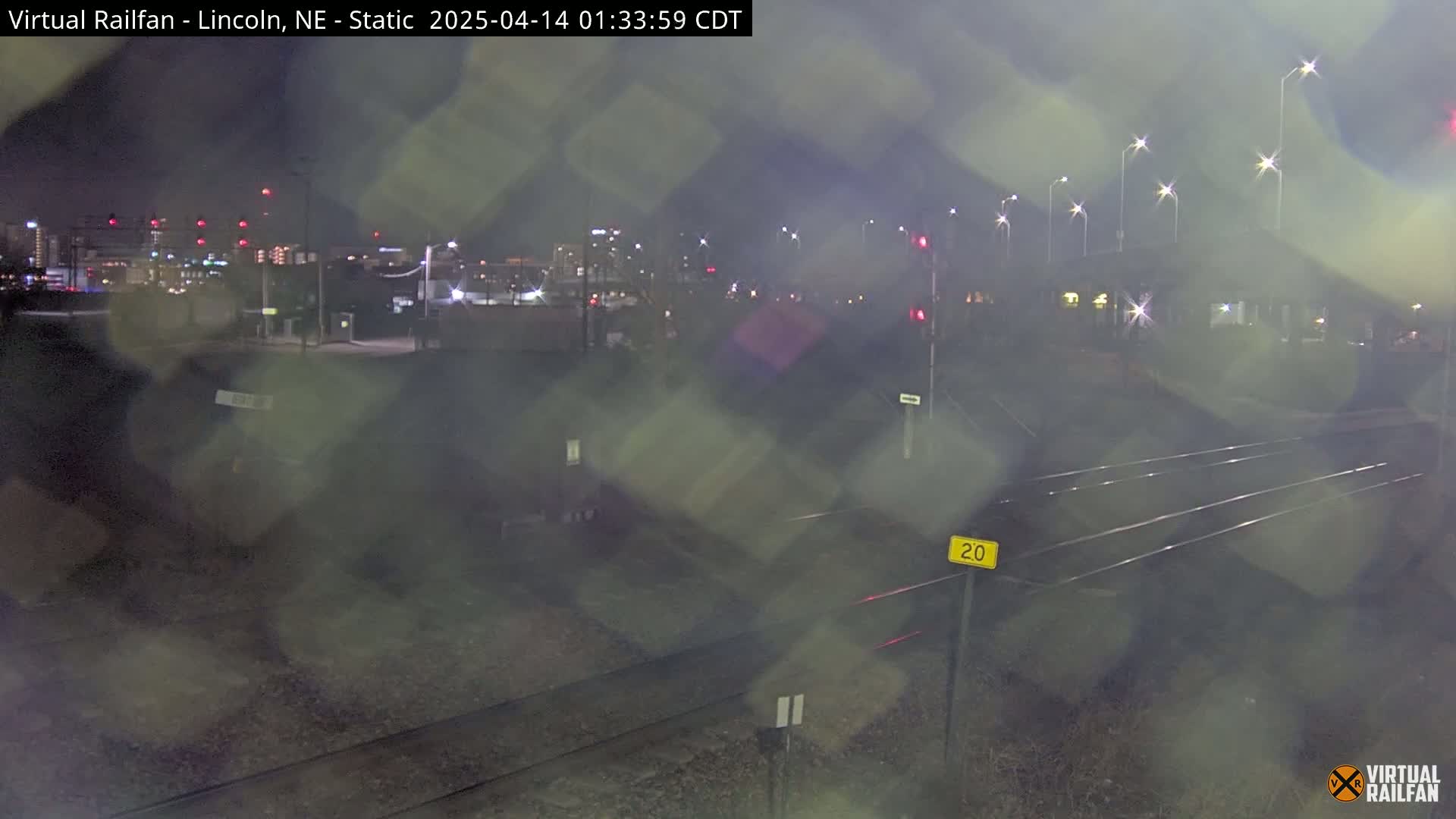 A nighttime view of railroad tracks and a city skyline in the distance, obscured by rain or fog.