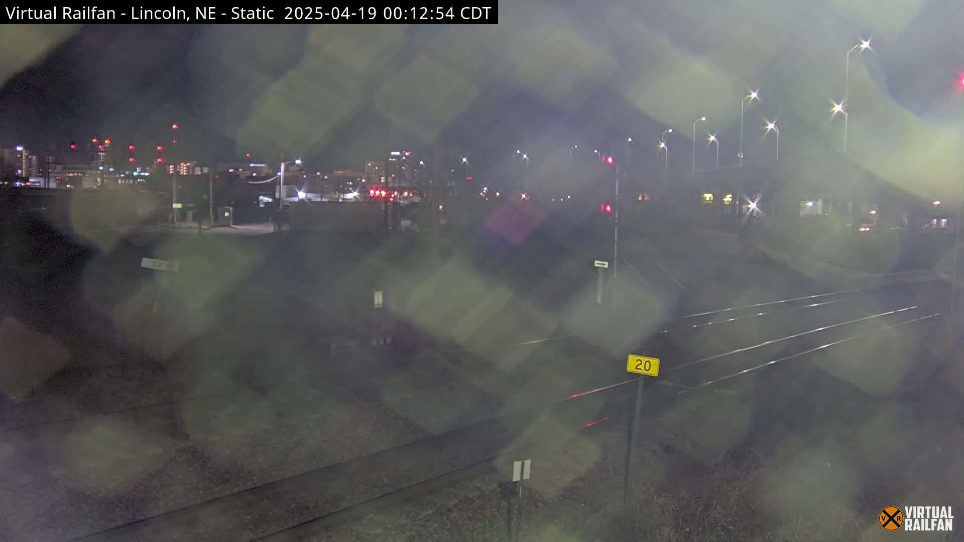 A nighttime view of train tracks and a city in the distance, with rain obscuring the view.