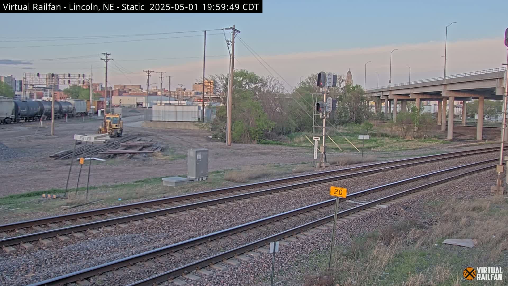 Railroad tracks and a train car are visible near a highway overpass under a twilight sky.