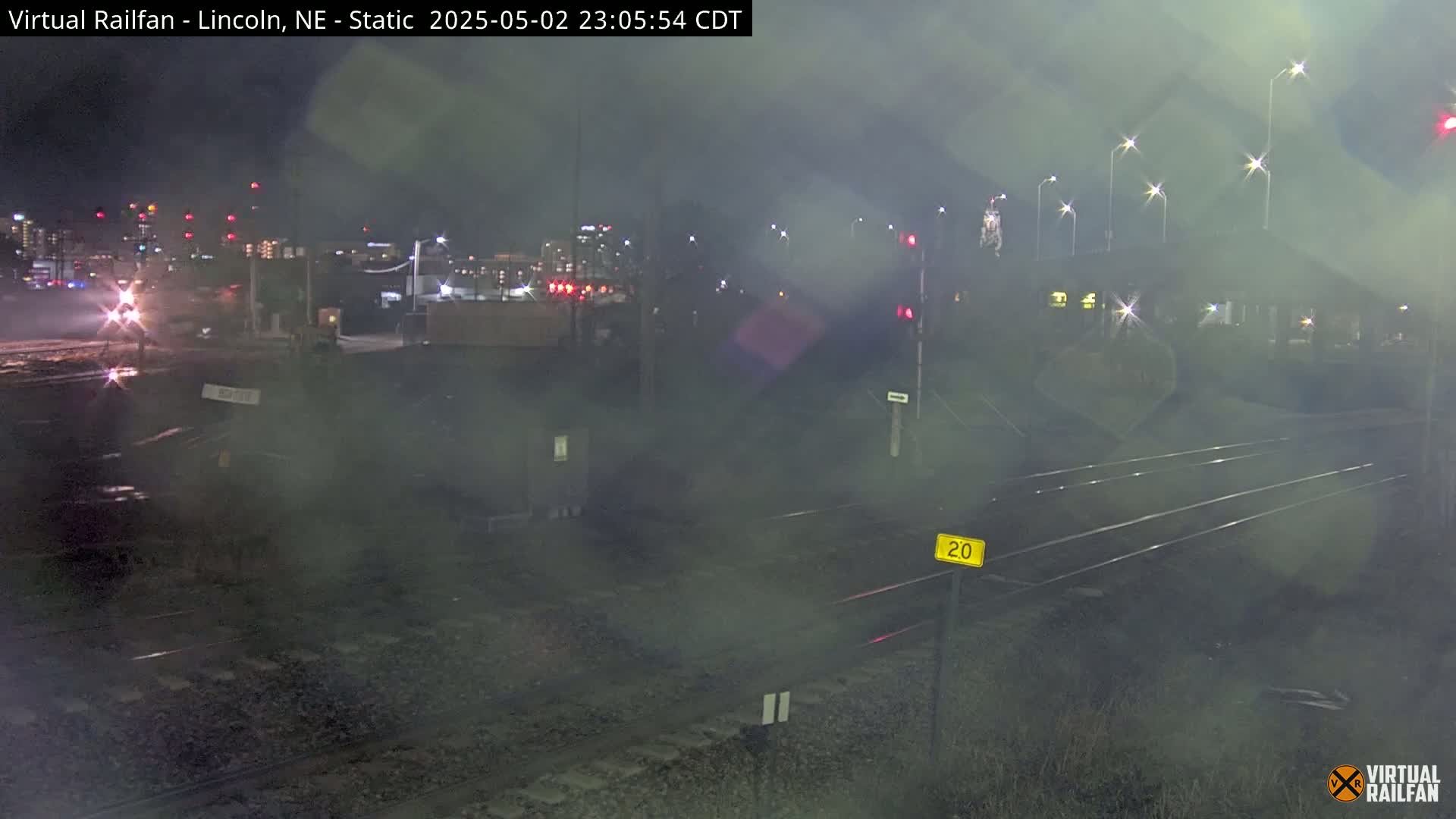 A nighttime, foggy view of railroad tracks with a city skyline in the background.