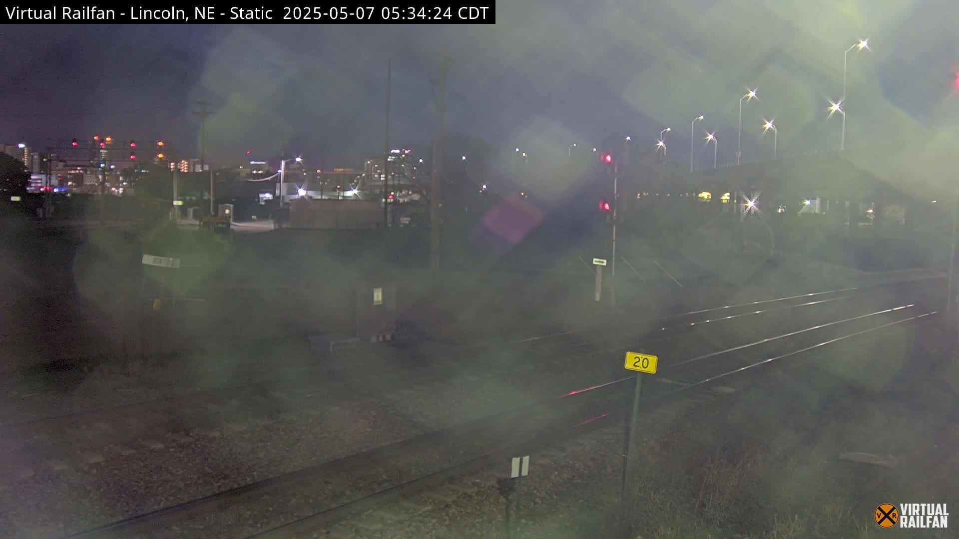 A nighttime view of railroad tracks and a distant city skyline under hazy conditions.