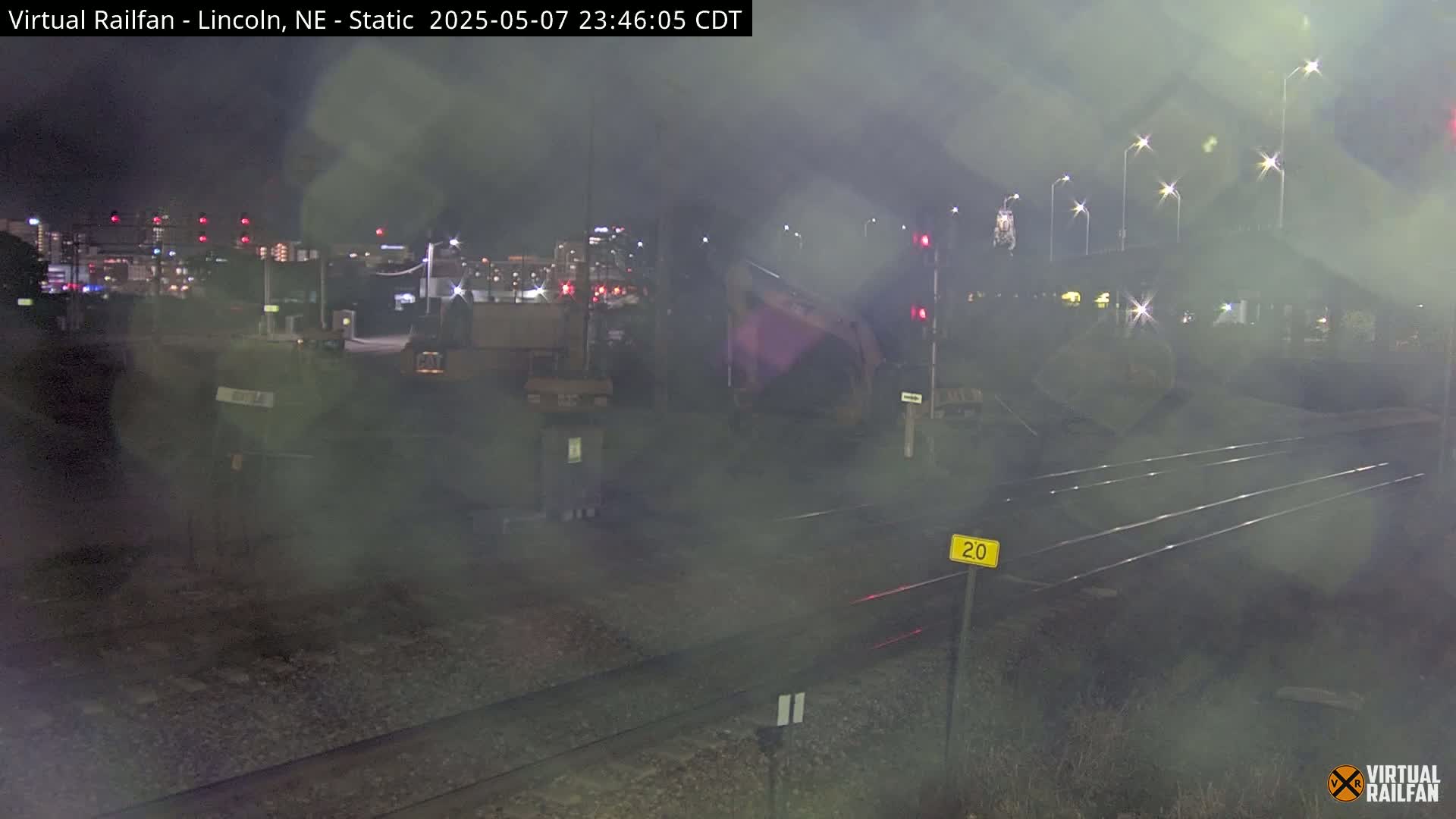 A nighttime view of railroad tracks and a distant city skyline under hazy conditions.