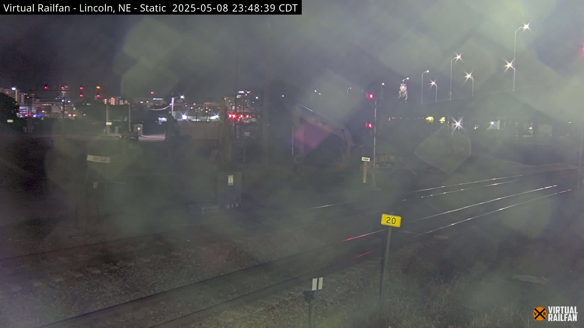 A nighttime view of railroad tracks under hazy conditions, with a distant city skyline illuminated.