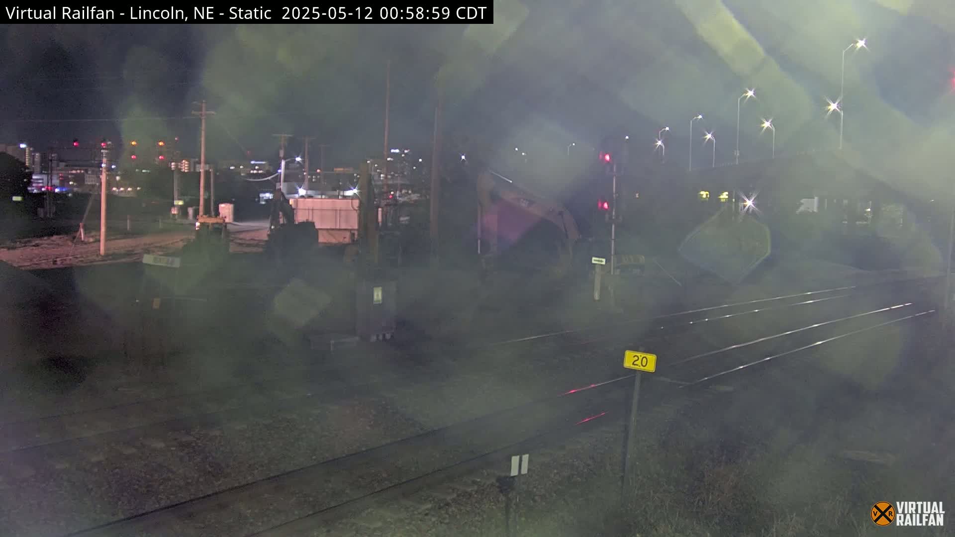 A nighttime view of a construction site near railroad tracks, with hazy or foggy conditions.