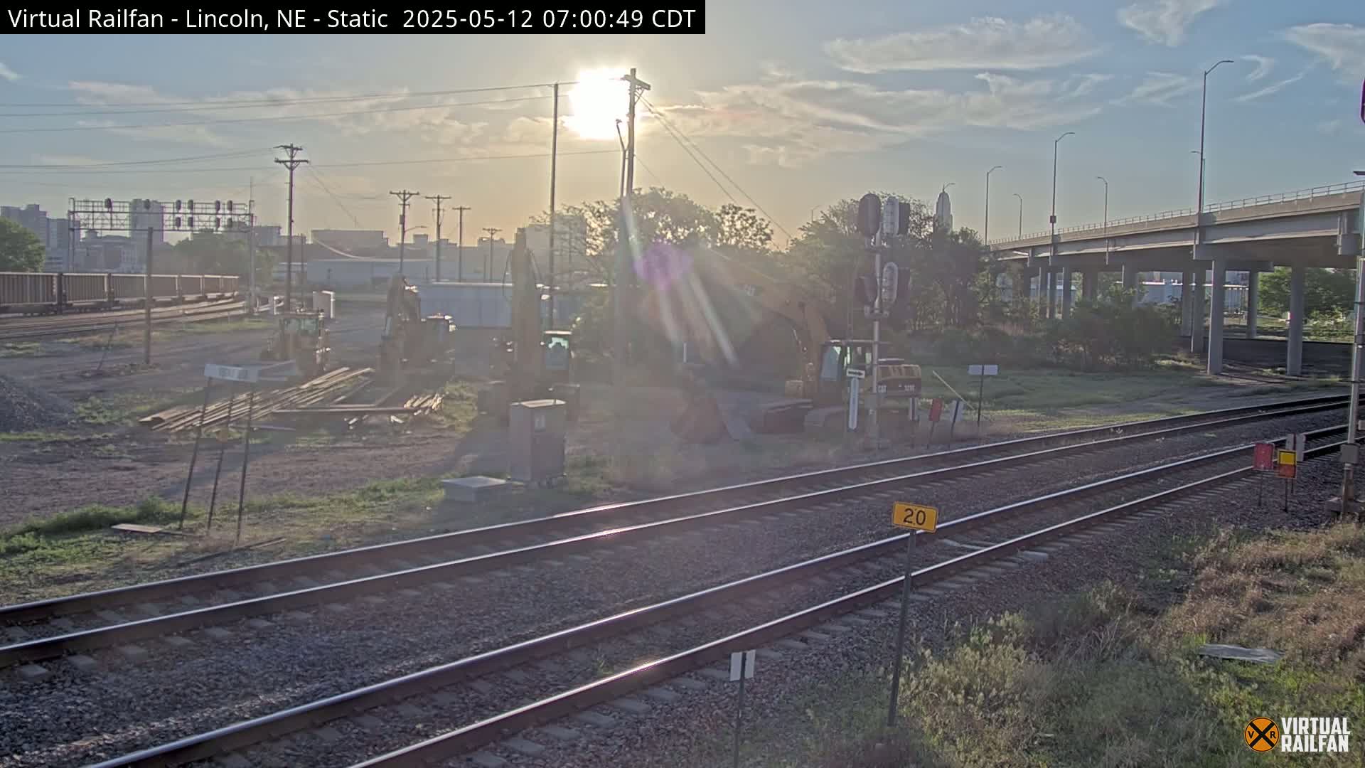 Construction equipment sits near railroad tracks under a partly sunny sky.