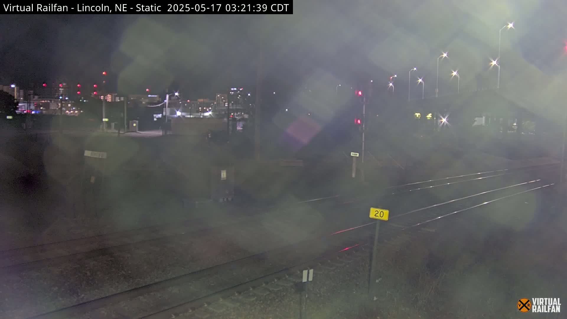 A nighttime view of railroad tracks under a hazy sky, with distant city lights visible in the background.