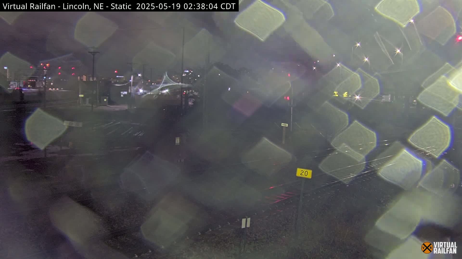 A nighttime view of railroad tracks and a city skyline, obscured by rain or some other form of precipitation.