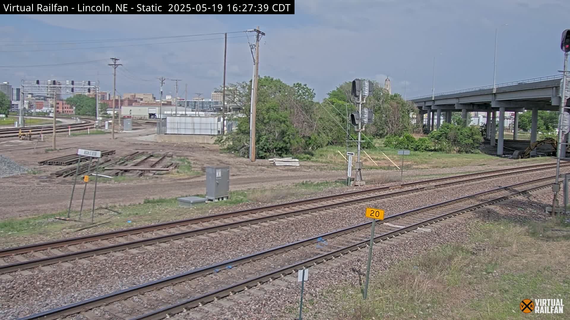 A view of railroad tracks and a cityscape in the distance under a partly cloudy sky.