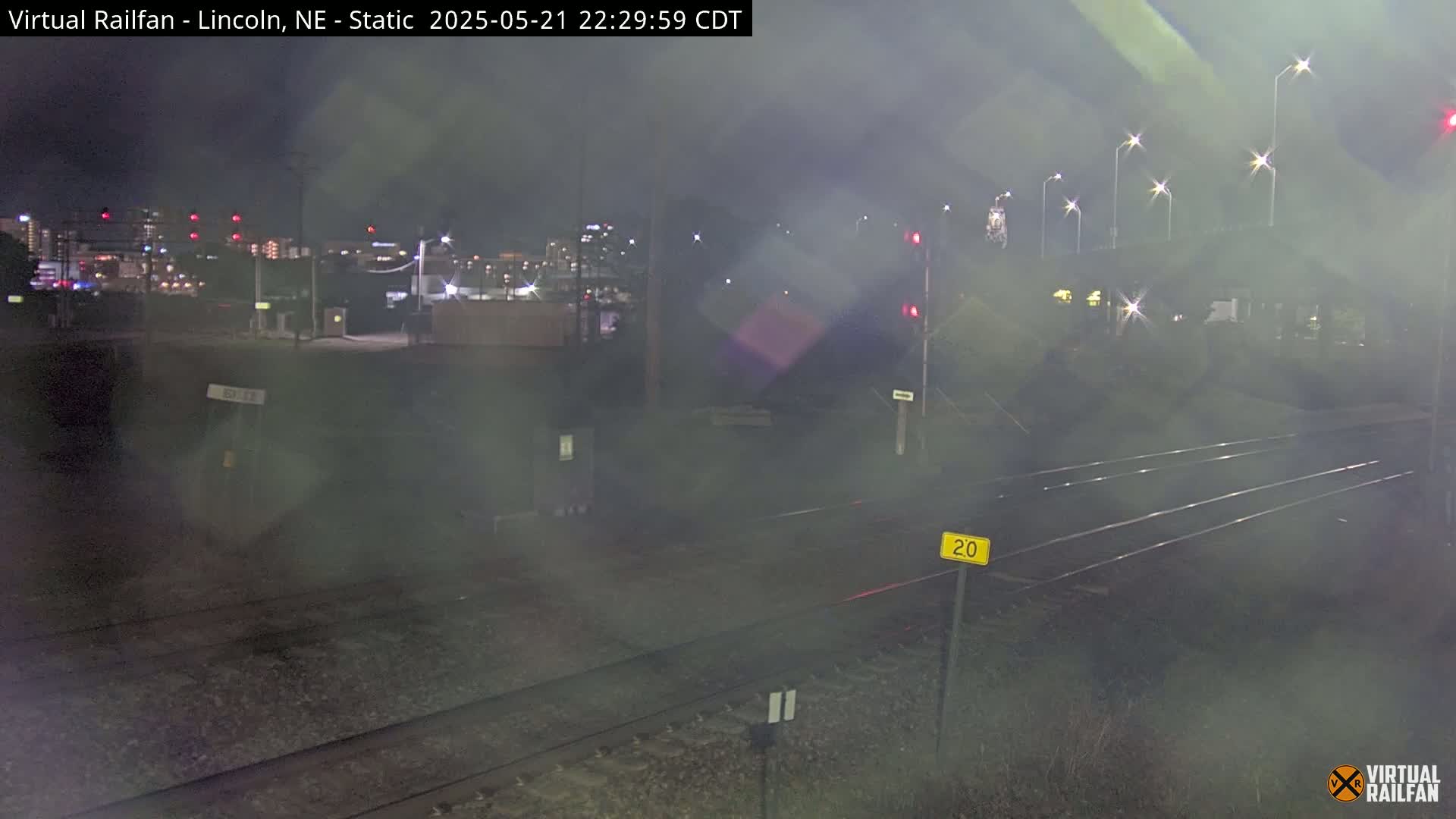 A nighttime view of railroad tracks, with a hazy or foggy atmosphere, and city lights in the distance.