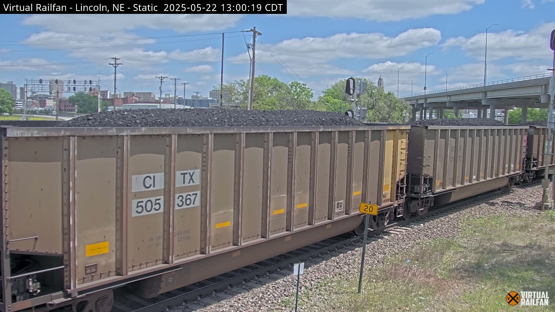 A long train carrying coal sits on the tracks under a partly cloudy sky.