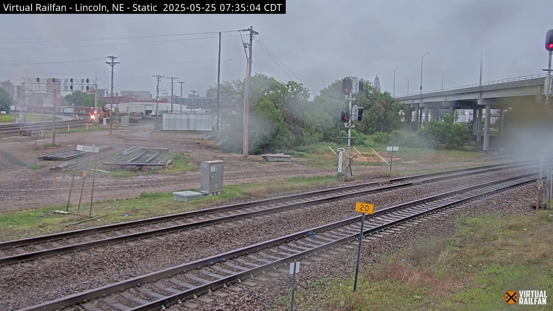 A train is visible in the distance on a set of railroad tracks, under a hazy, overcast sky.