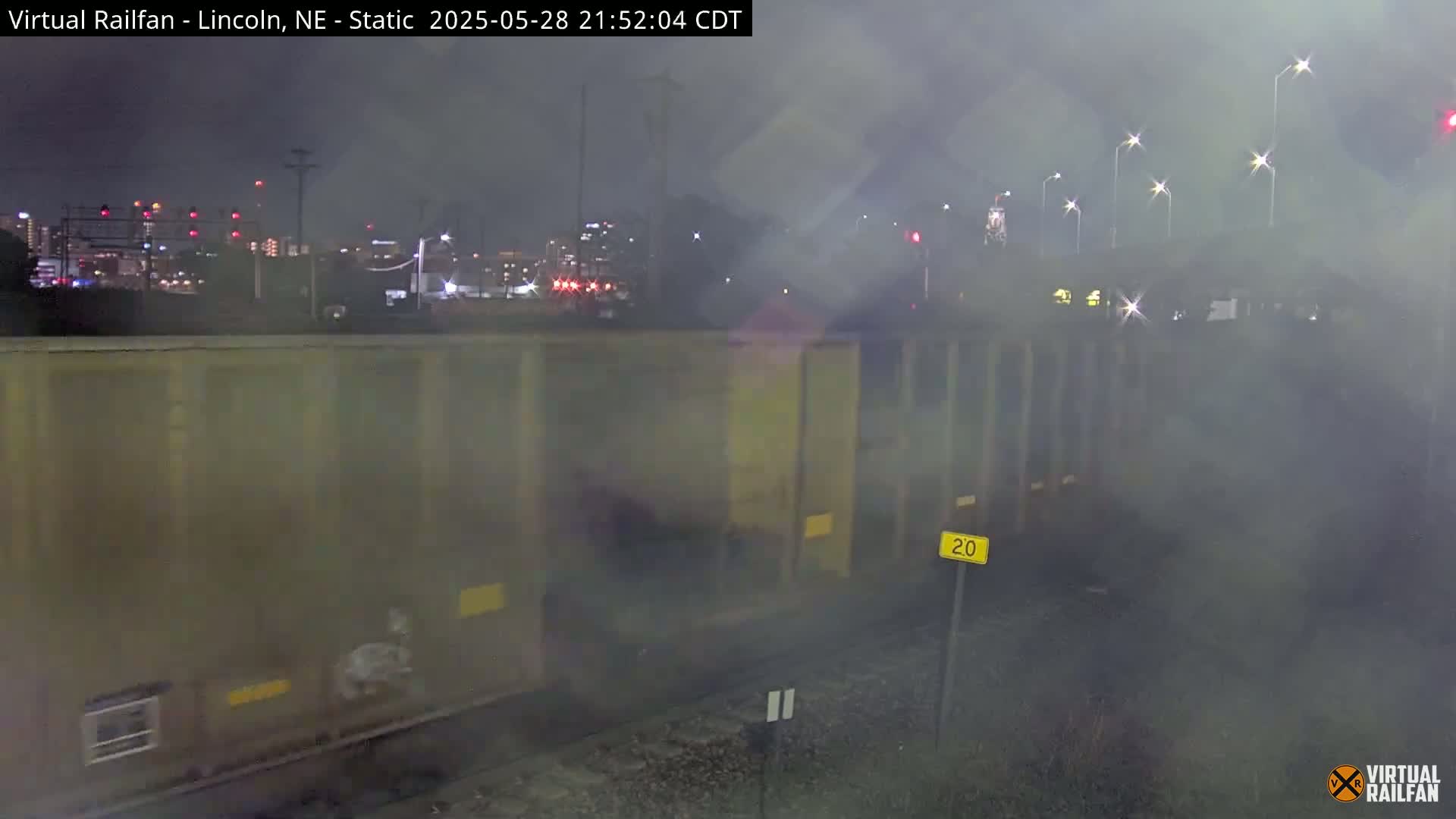 A nighttime view of a freight train car near a city skyline under hazy or foggy conditions.