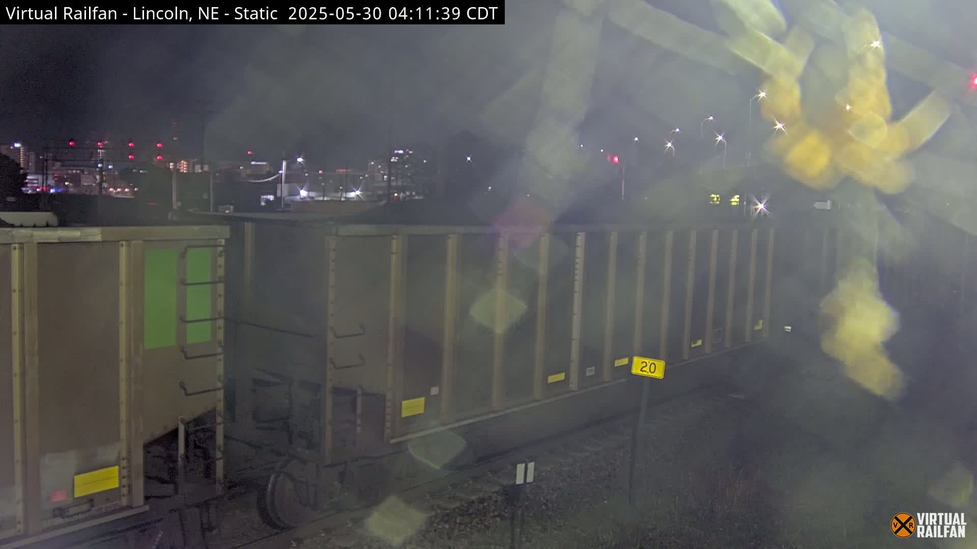 A nighttime view of several boxcars on a train track with a city skyline faintly visible in the background.