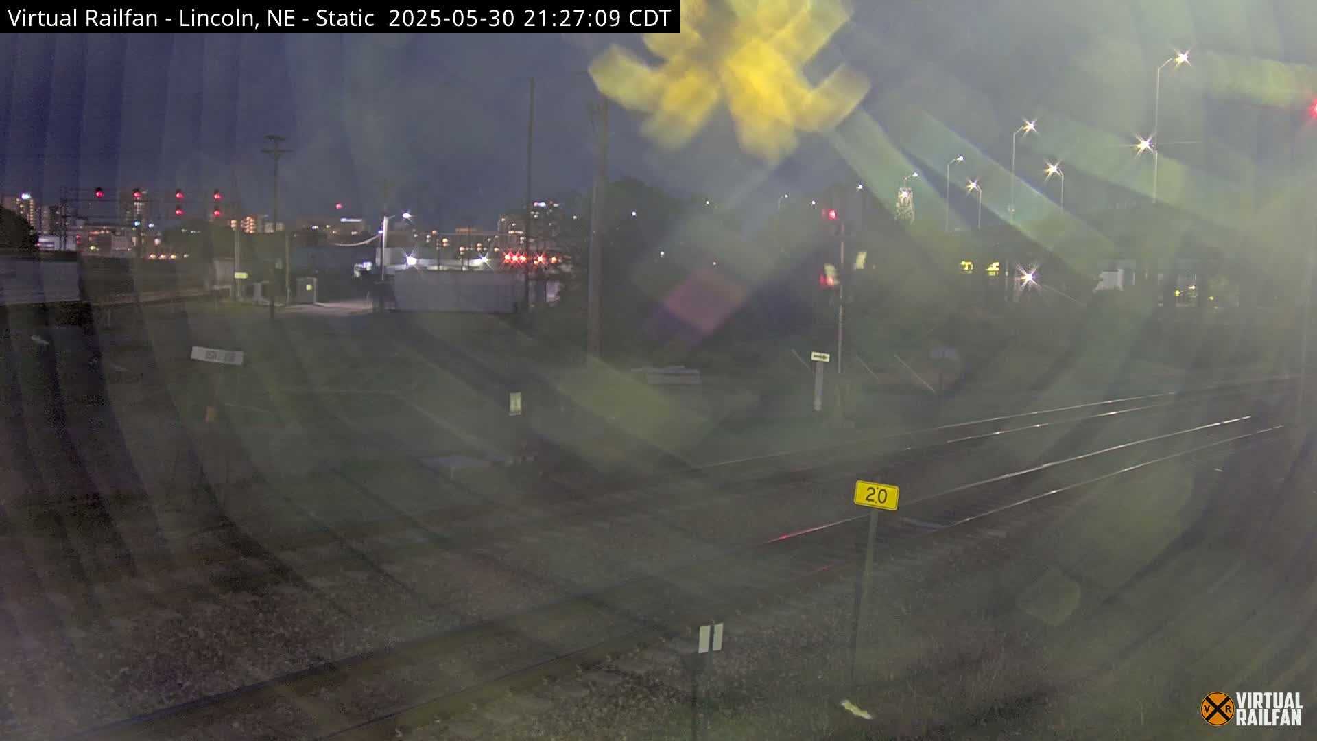 A nighttime view of railroad tracks and a cityscape in the distance, under dark skies.