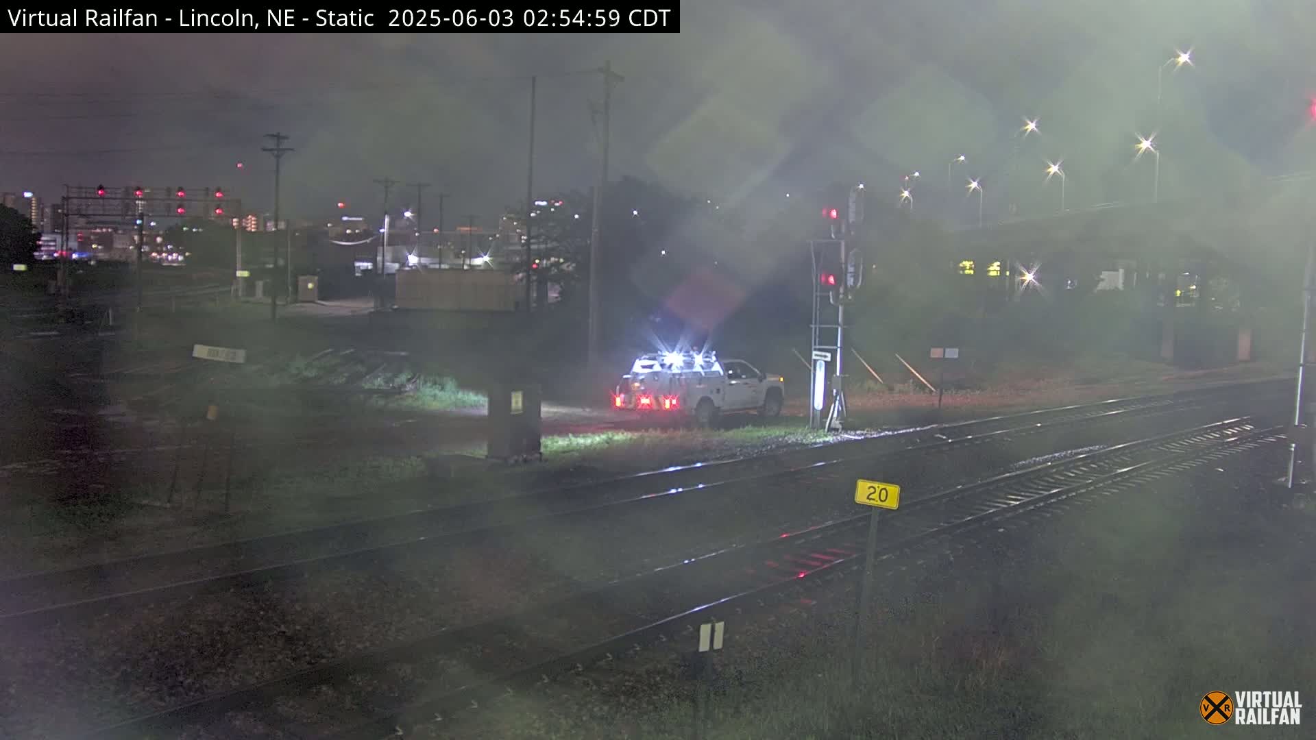 A white pickup truck is parked near railroad tracks at night under hazy conditions.