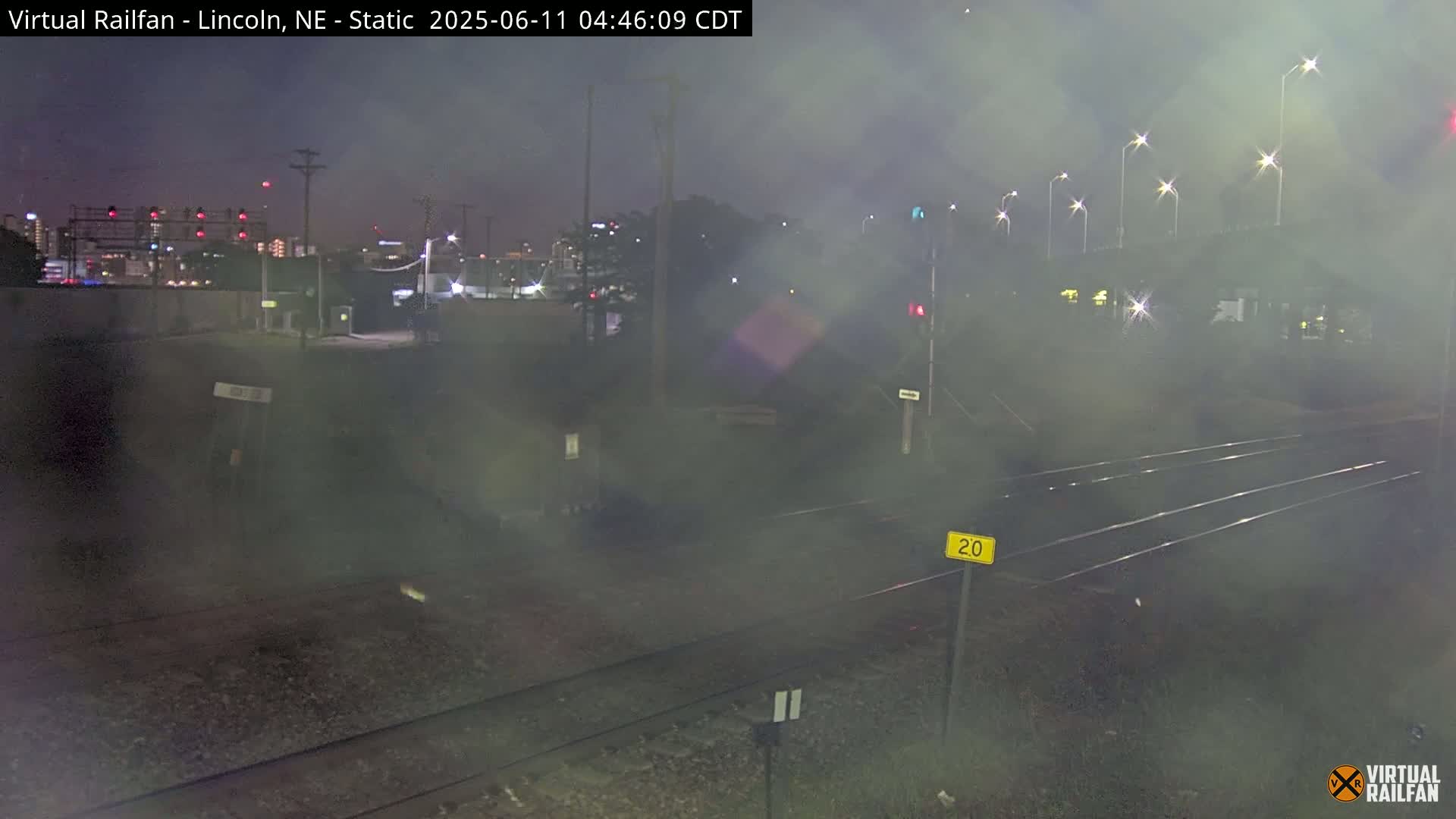 A nighttime, hazy view of railroad tracks and a distant city skyline.