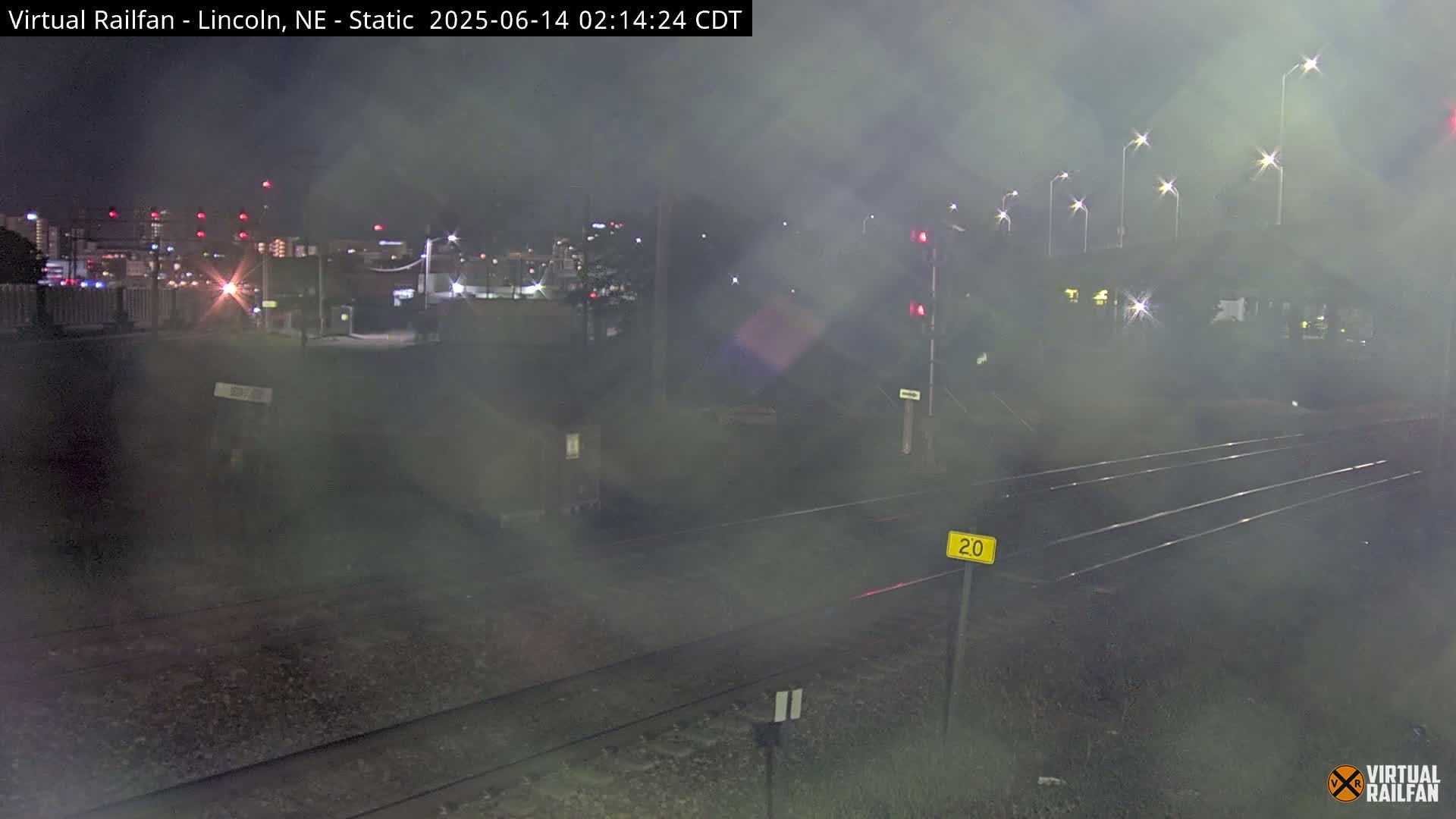 A nighttime view of railroad tracks leading toward a hazy city skyline under a foggy sky.