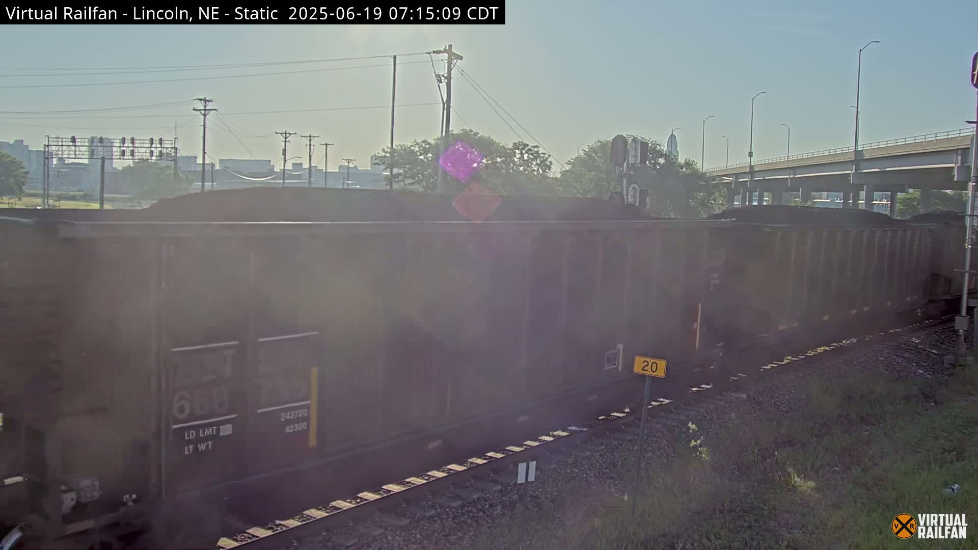 A long freight train carrying coal sits on railroad tracks under a clear, sunny sky.