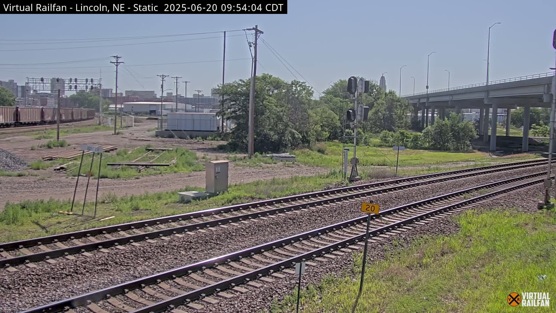 A train track with a distant cityscape under a clear sky, passing under a highway overpass.