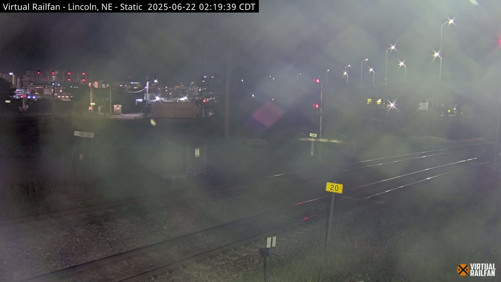 A nighttime view of railroad tracks leading toward a hazy city skyline under foggy conditions.