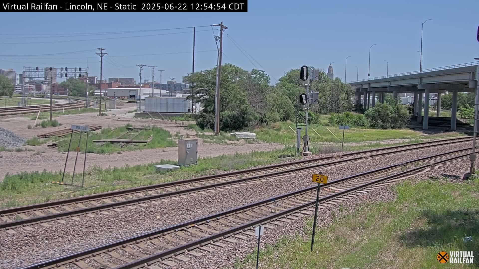 Railroad tracks run alongside a highway overpass under a mostly clear sky.